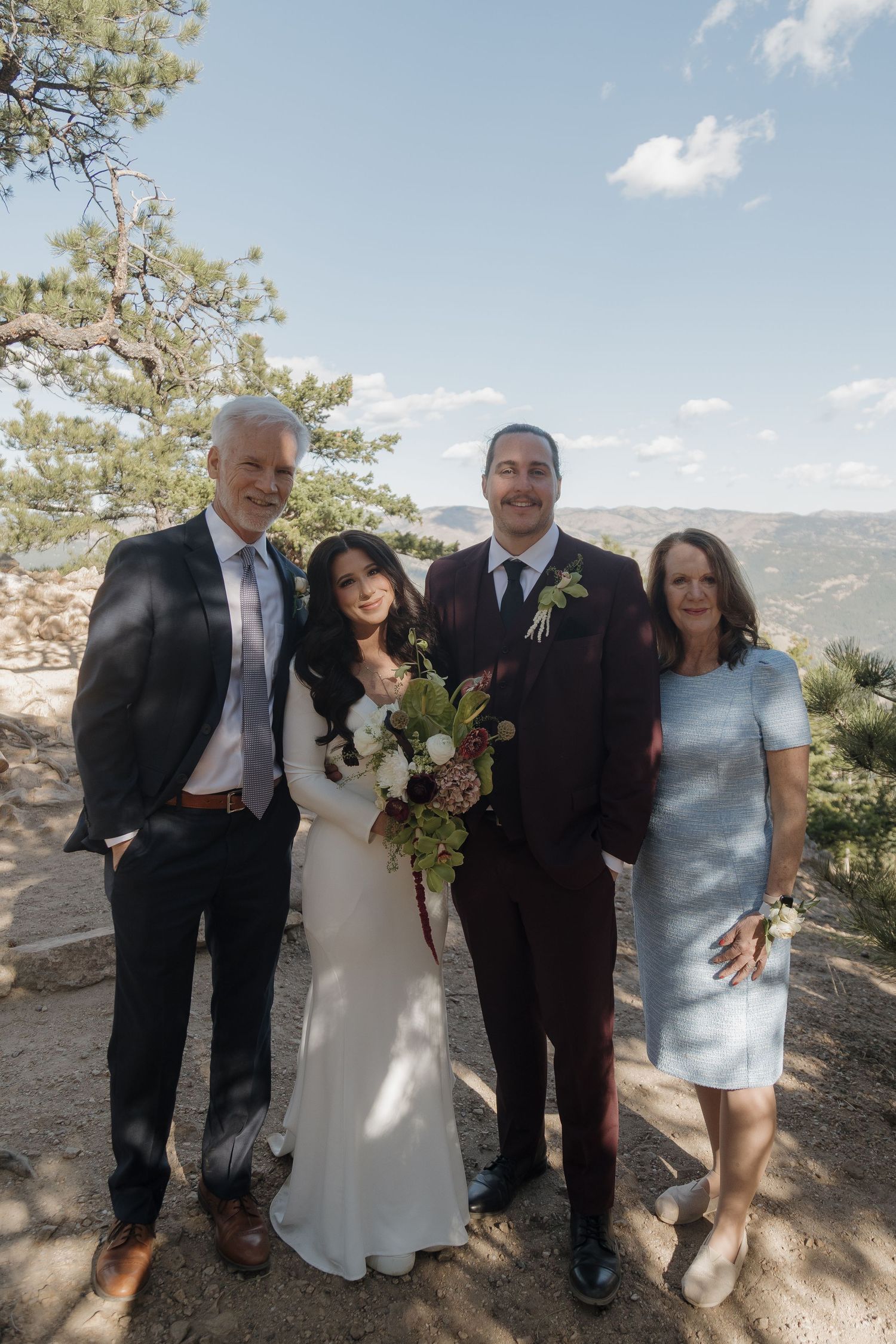 Bride and groom posing with family on mountain overlook, surrounded by pine trees and scenic valley views.