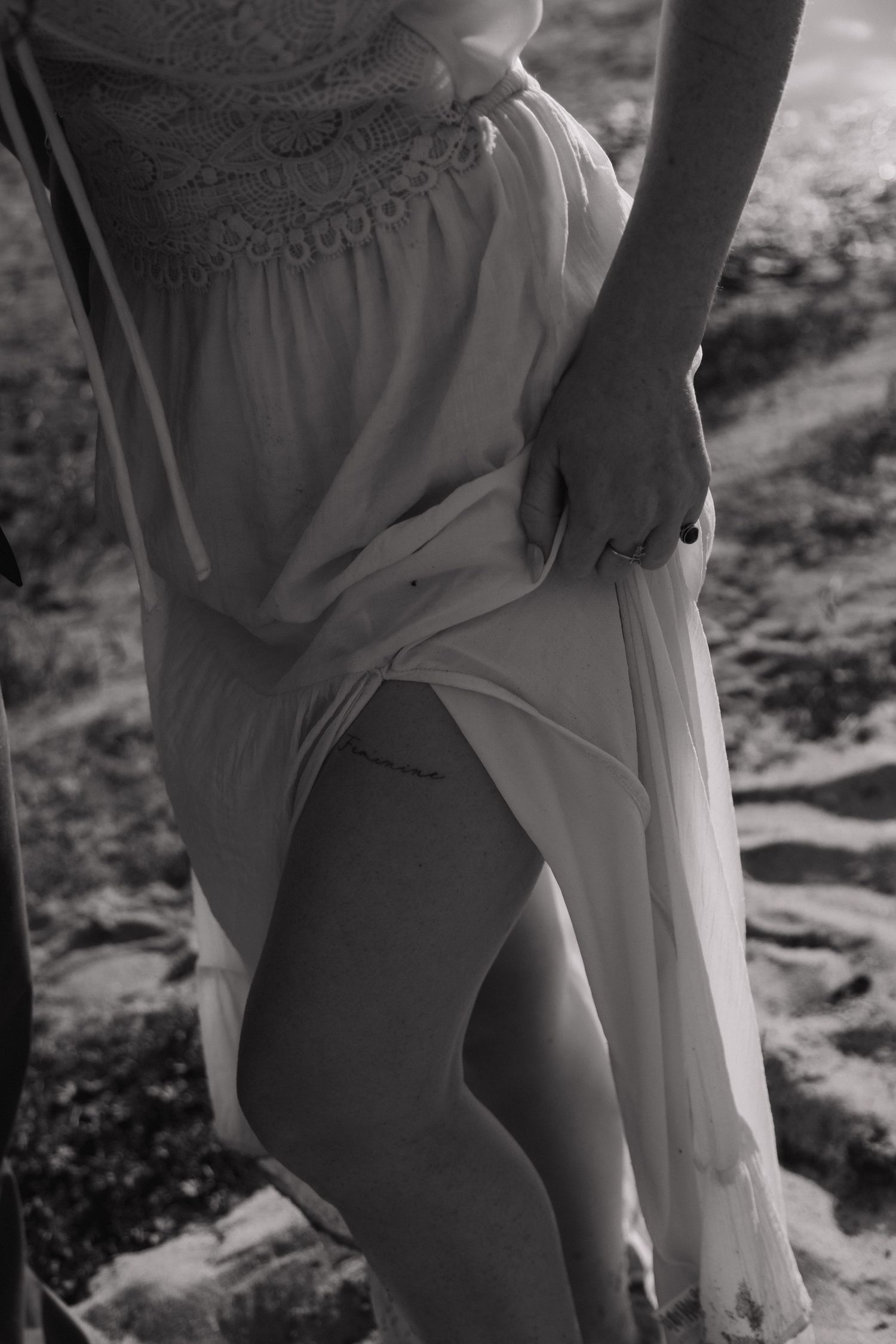Black and white photo of woman in flowing white dress holding hands with partner on rocky terrain.