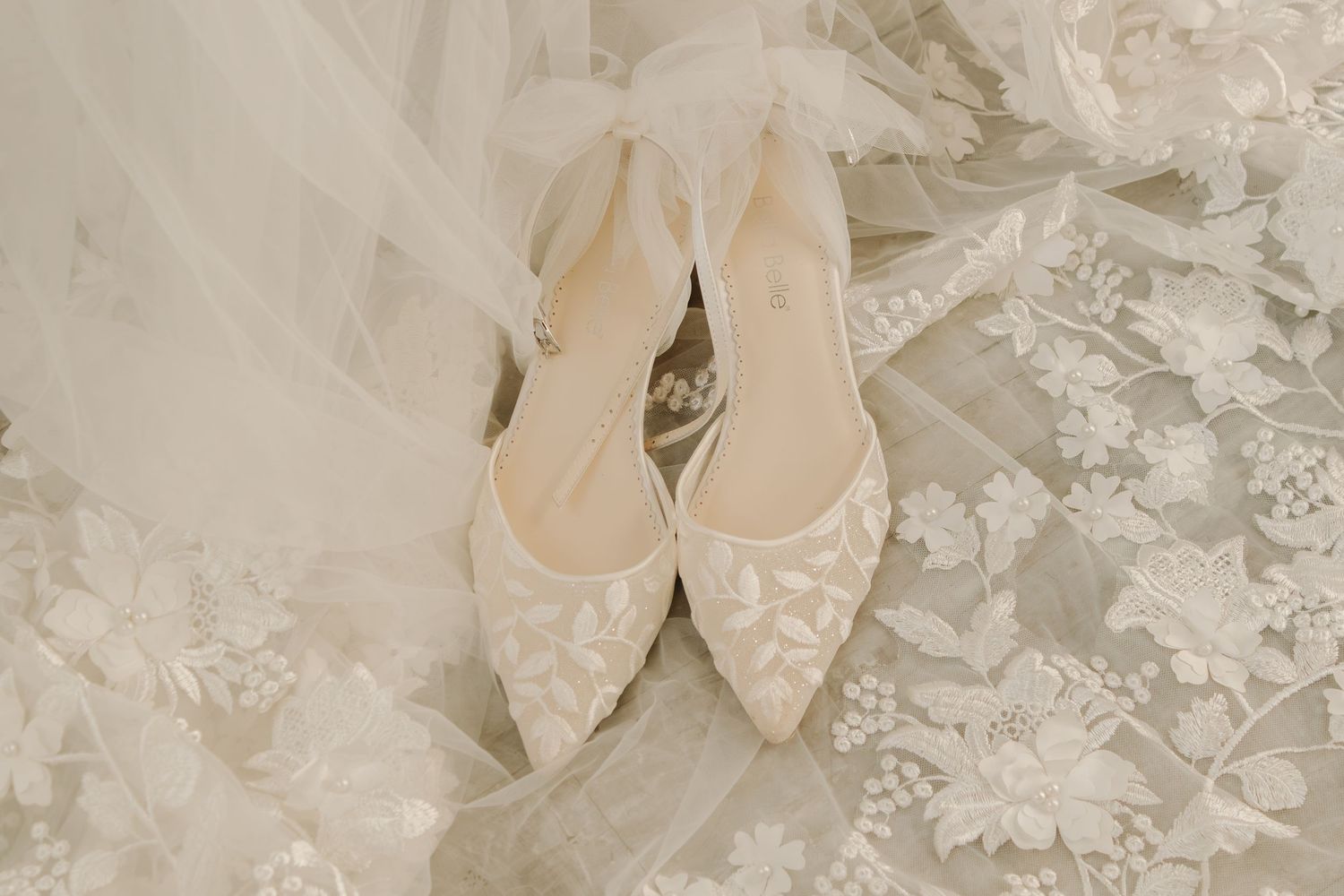 Elegant white lace bridal shoes displayed on delicate tulle fabric.