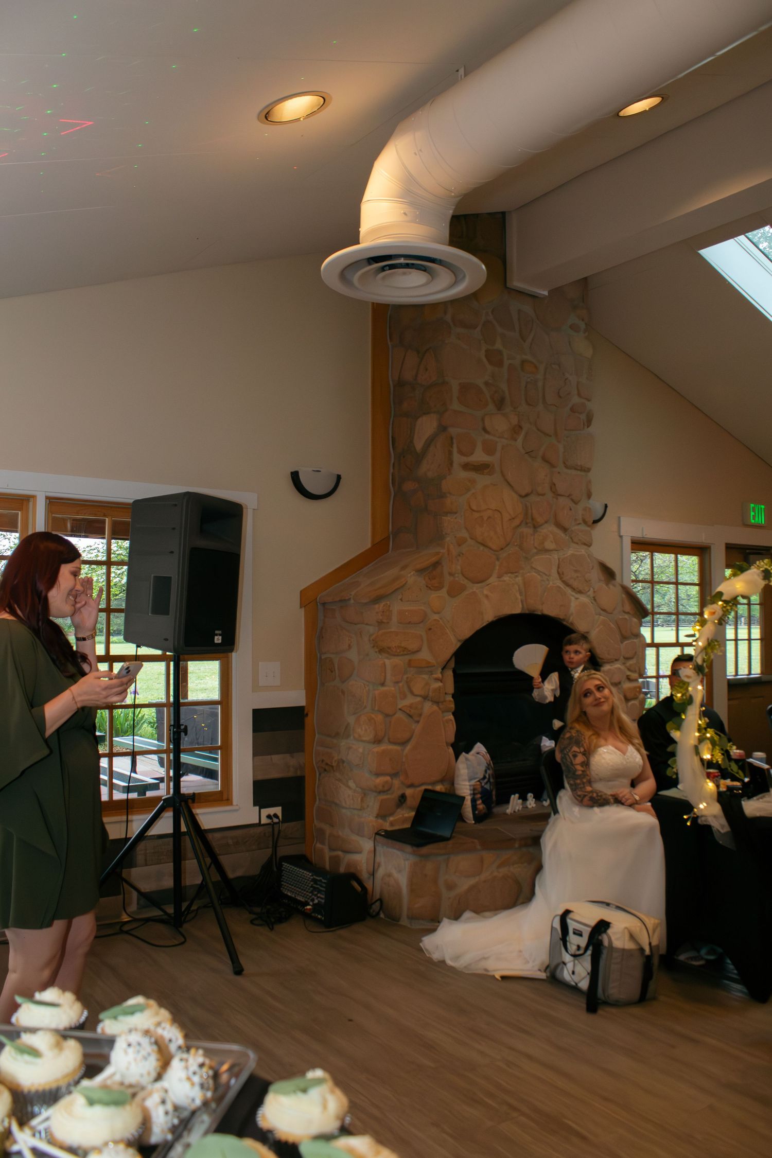 Wedding reception venue with stone fireplace, wooden floors, and cupcake display.