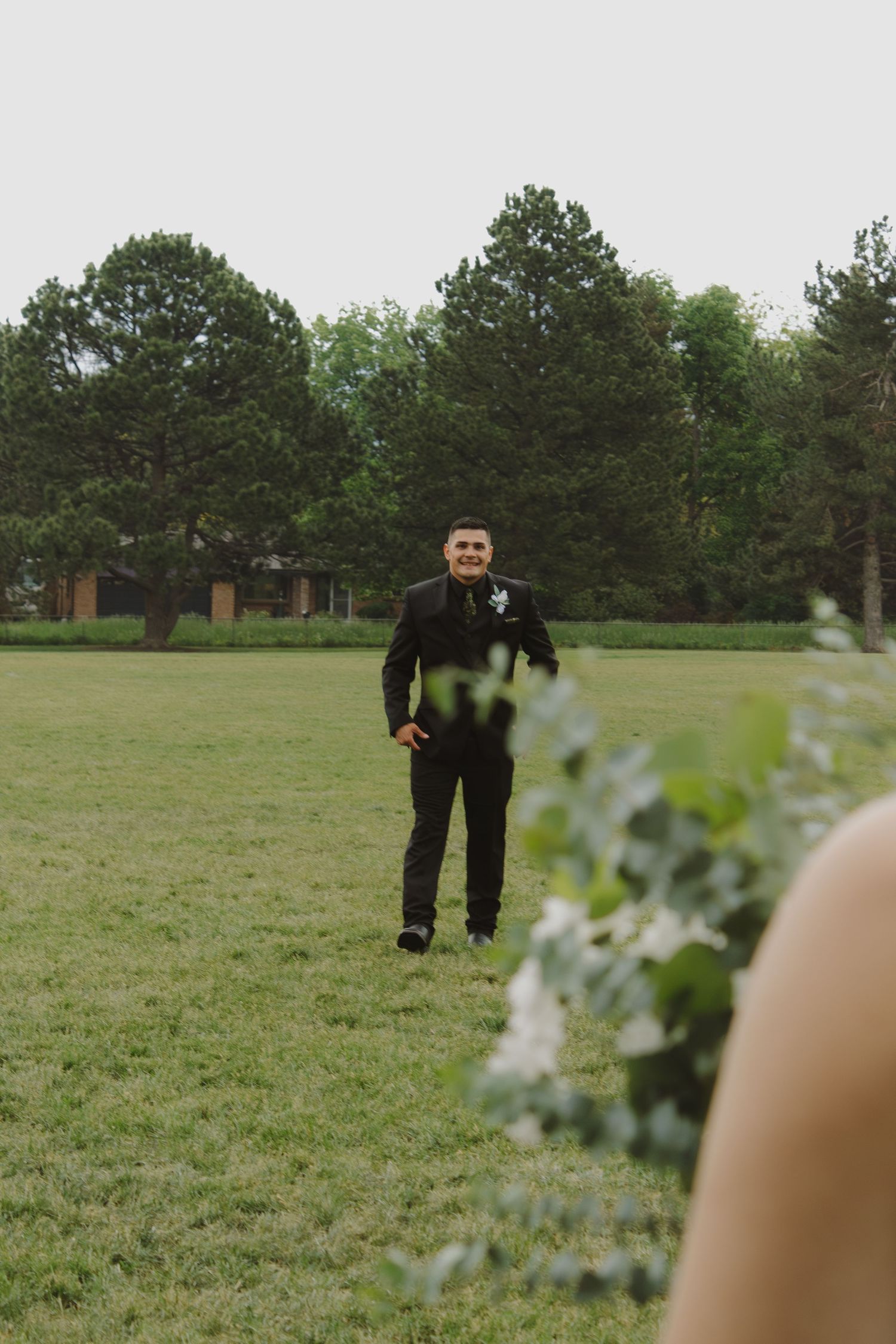 Groom standing in field waiting for first look with trees in background.