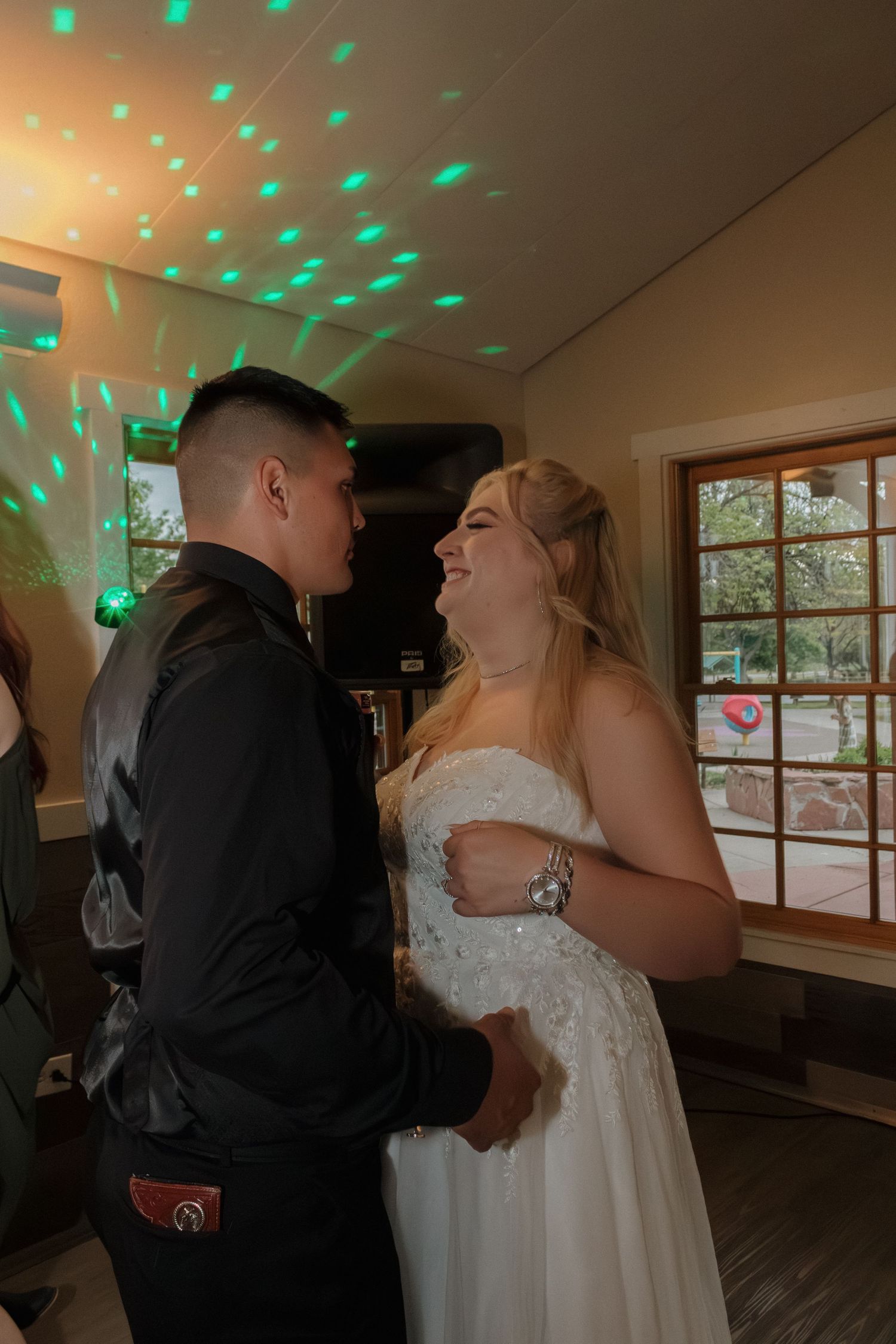 A couple sharing a romantic dance moment under green party lights at their wedding reception.