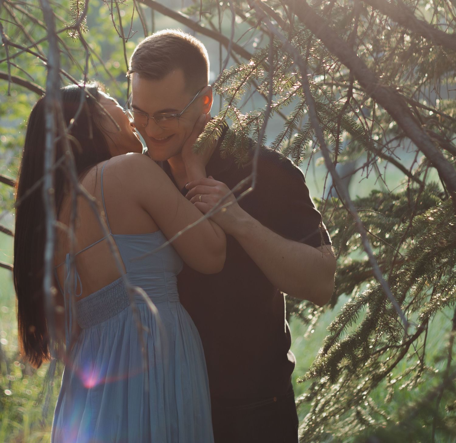 Sunlit forest scene with couple in tender embrace among tree branches.