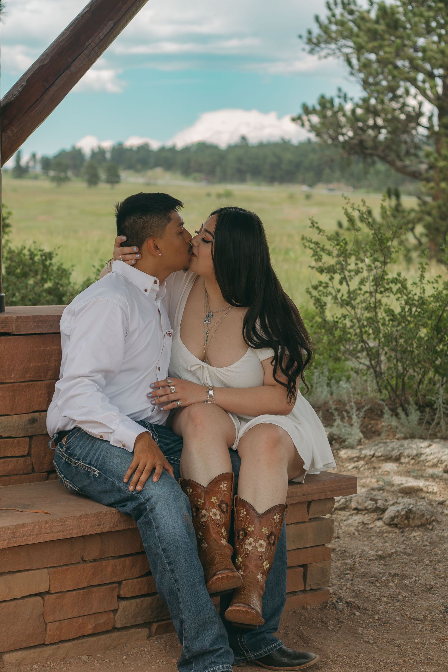 Couple sharing romantic moment on wooden bench with mountain landscape in background.