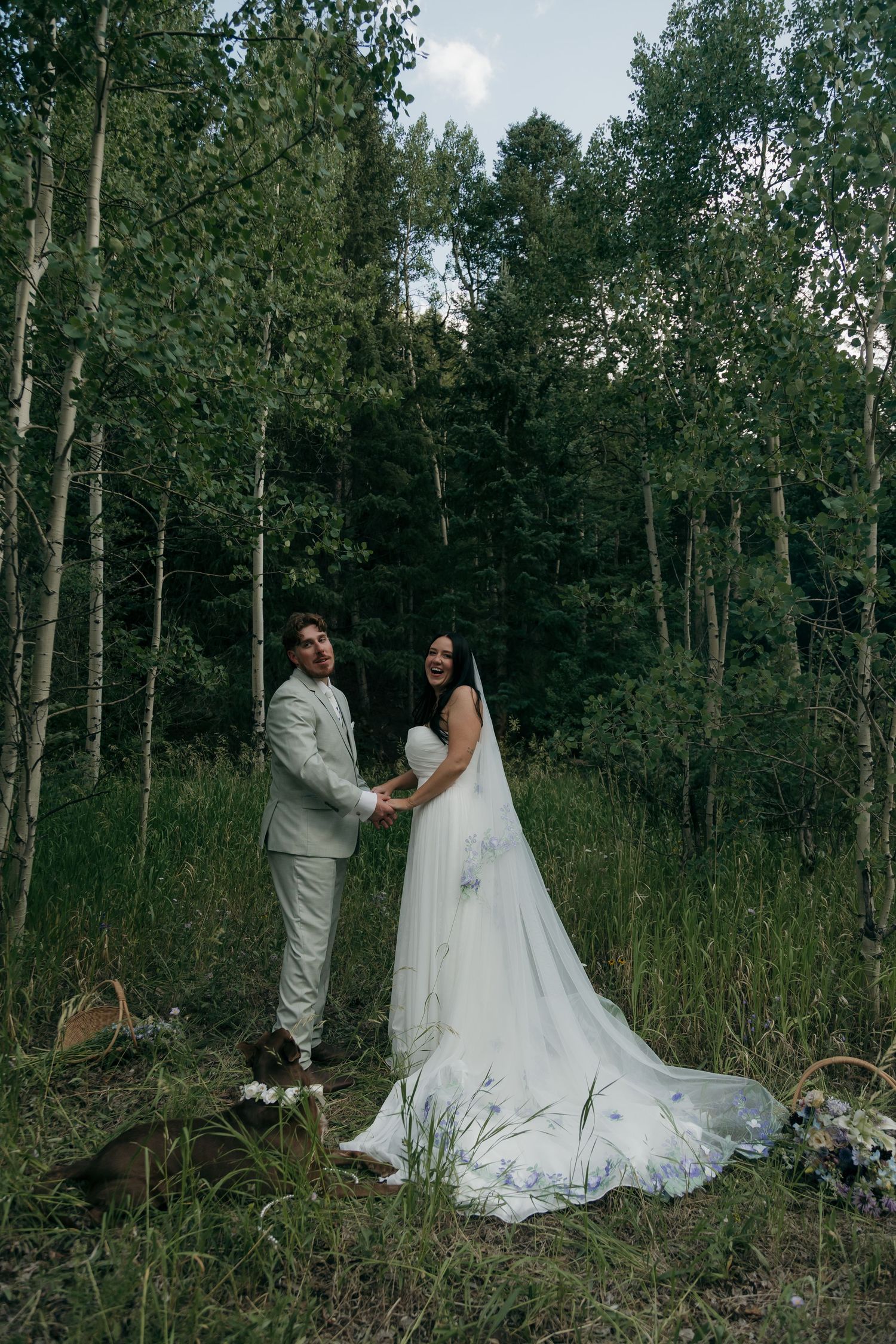Bride and groom laugh holding hands in aspen forest during outdoor elopement with their dog.