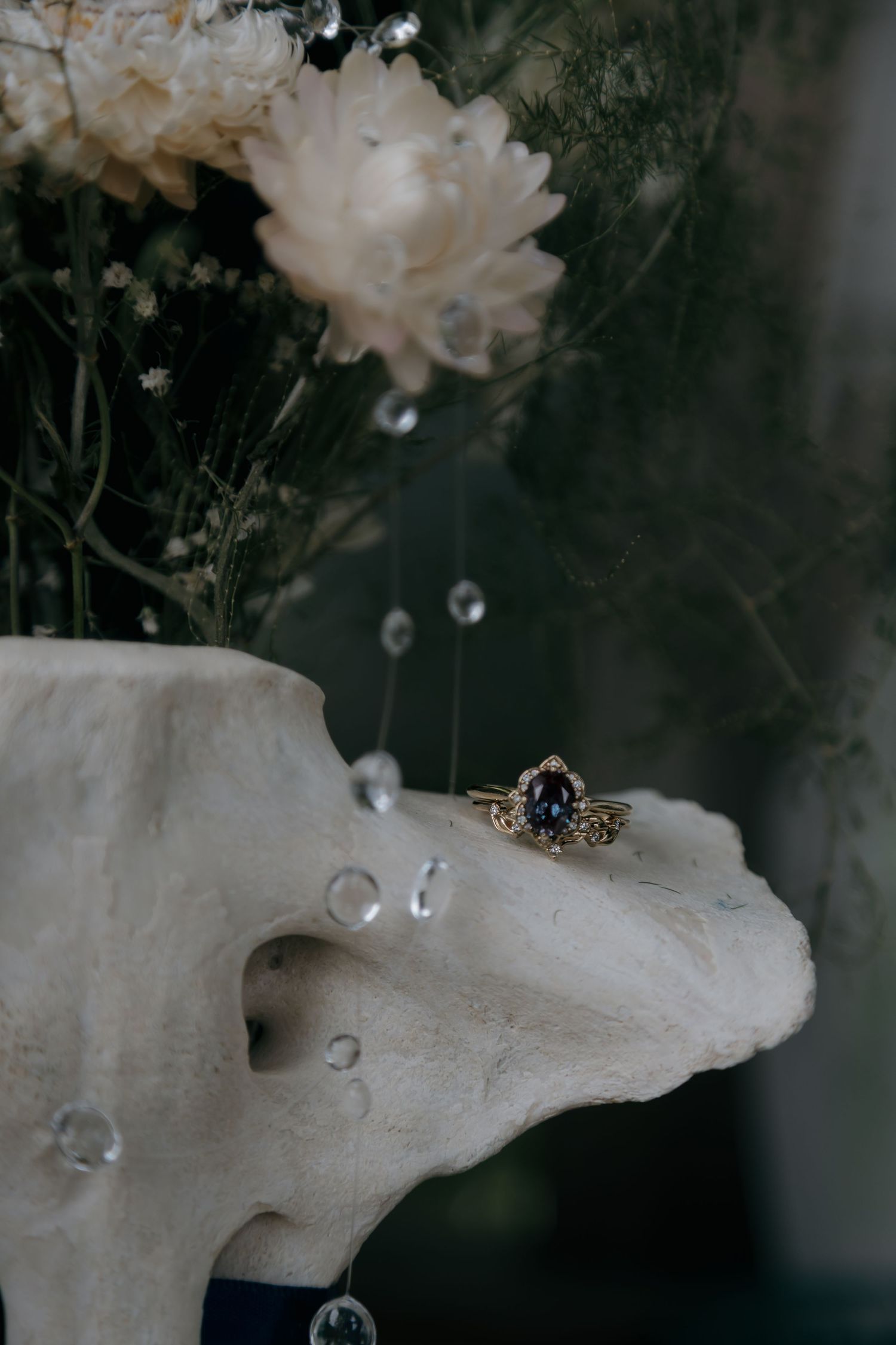 Elegant sapphire and diamond engagement ring resting on a white coral sculpture with crystal drops and white flowers.