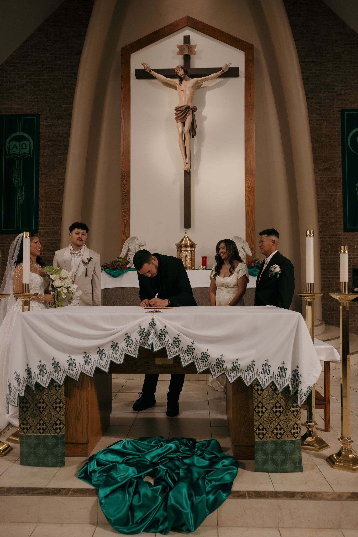 Groom signing wedding register at church altar with crucifix backdrop during Catholic ceremony.