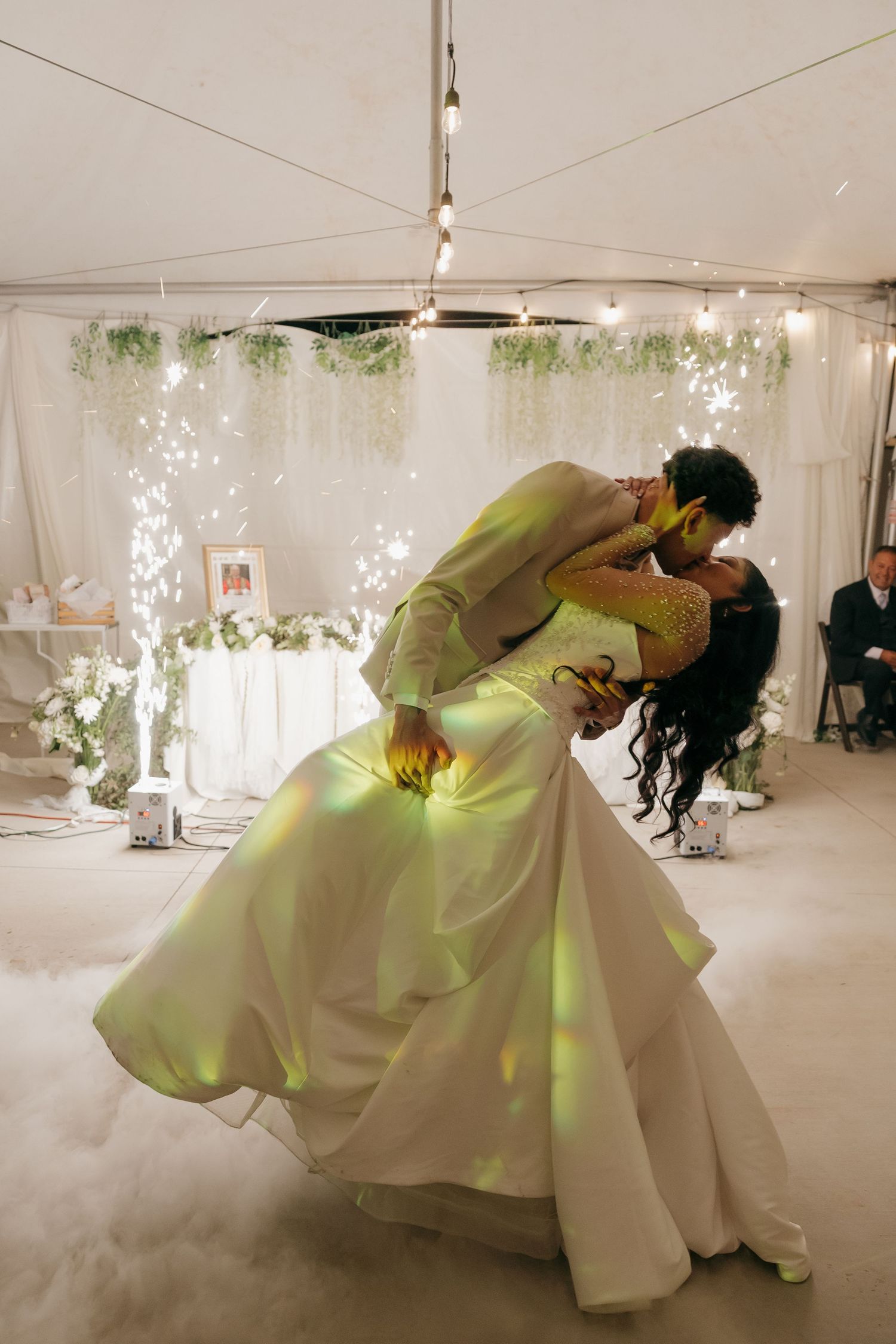 Groom dips bride during first dance under sparkling lights in a dreamy fog-filled tent.