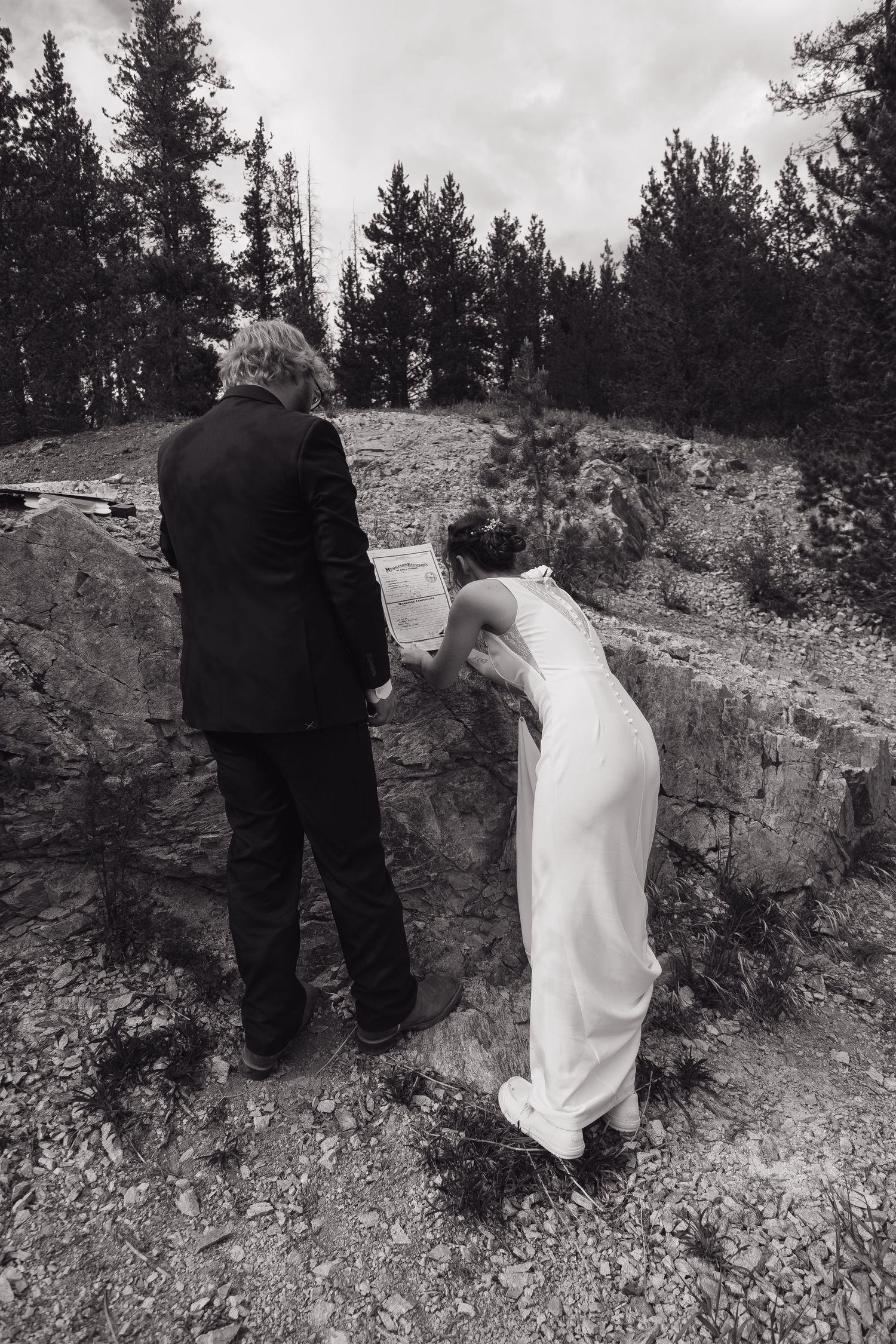 Bride and groom hold hands while exploring rocky terrain in wedding attire.