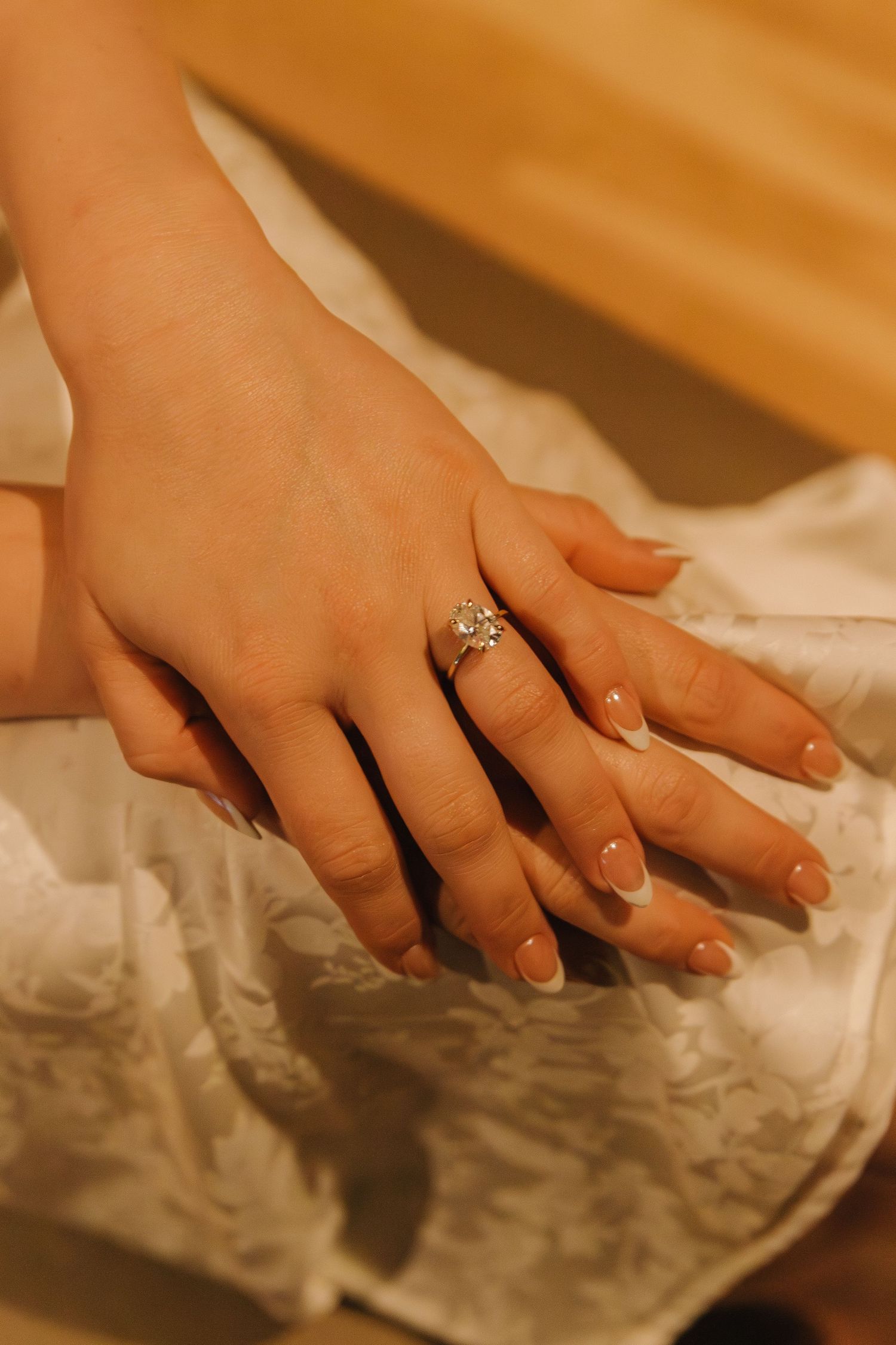 Close-up sequence of hands with an engagement ring resting on white fabric.