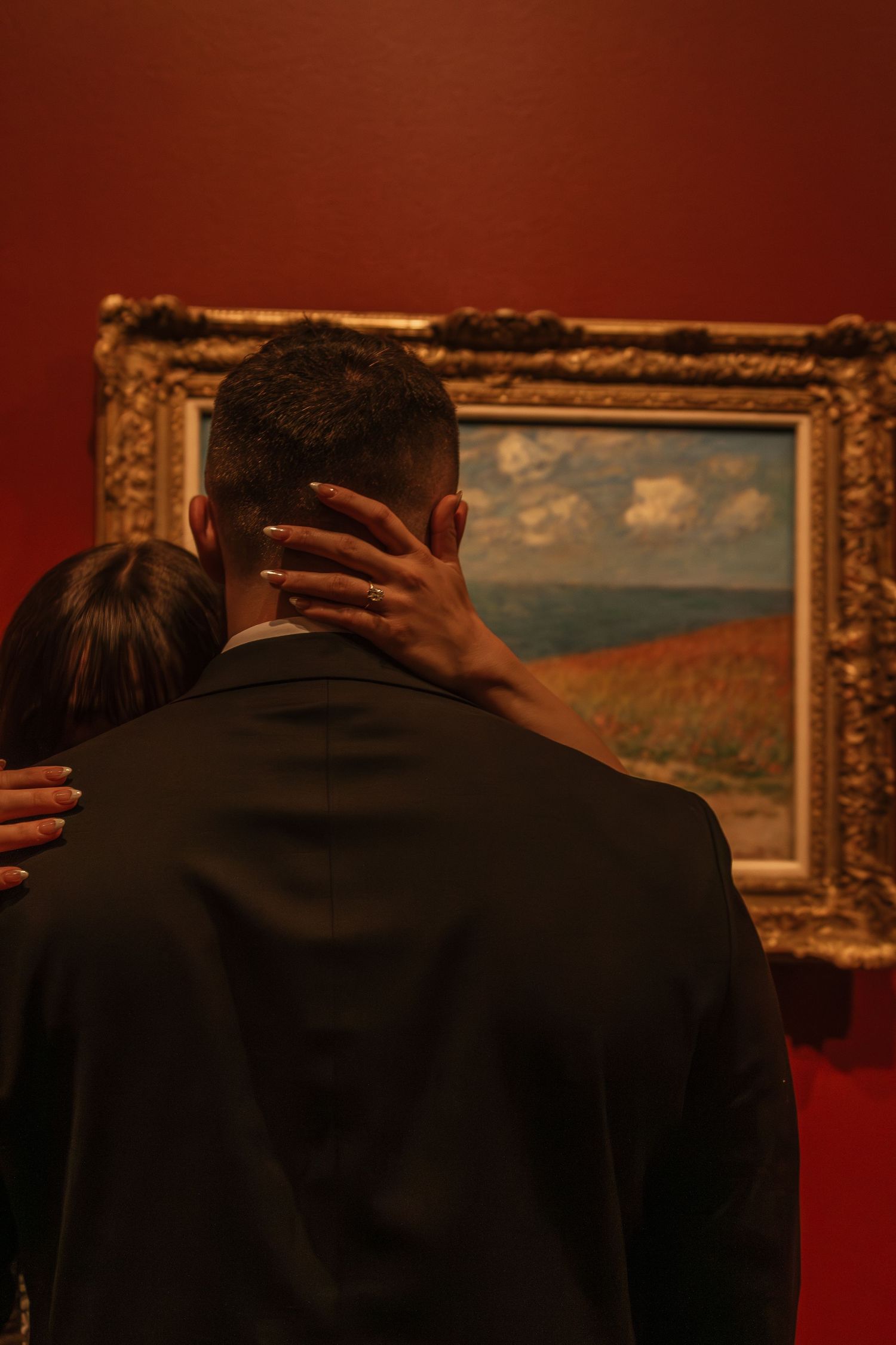 Art gallery wall with framed landscape paintings in ornate gold frames against deep red walls.