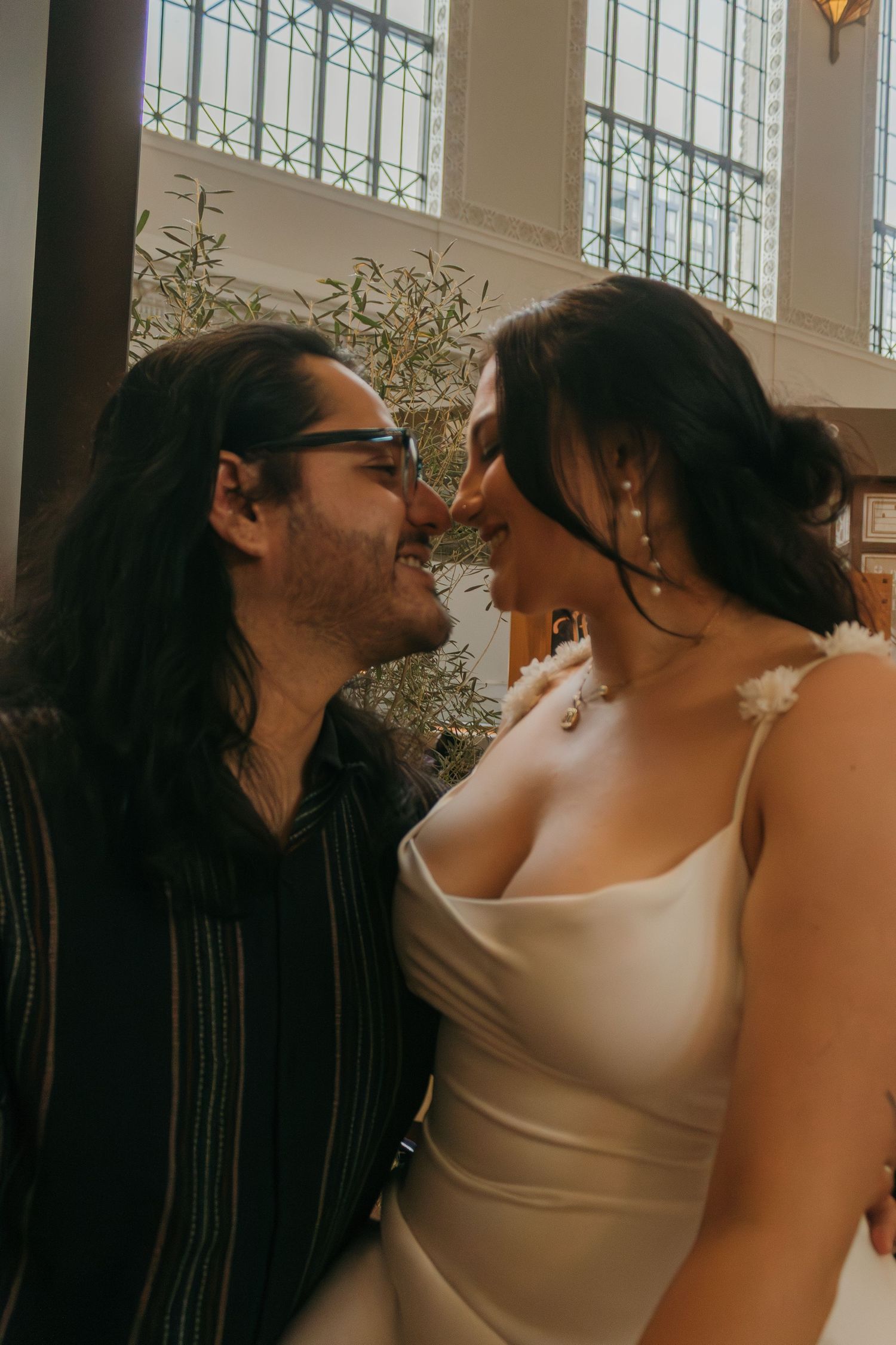 A couple shares an intimate moment in front of large industrial windows.