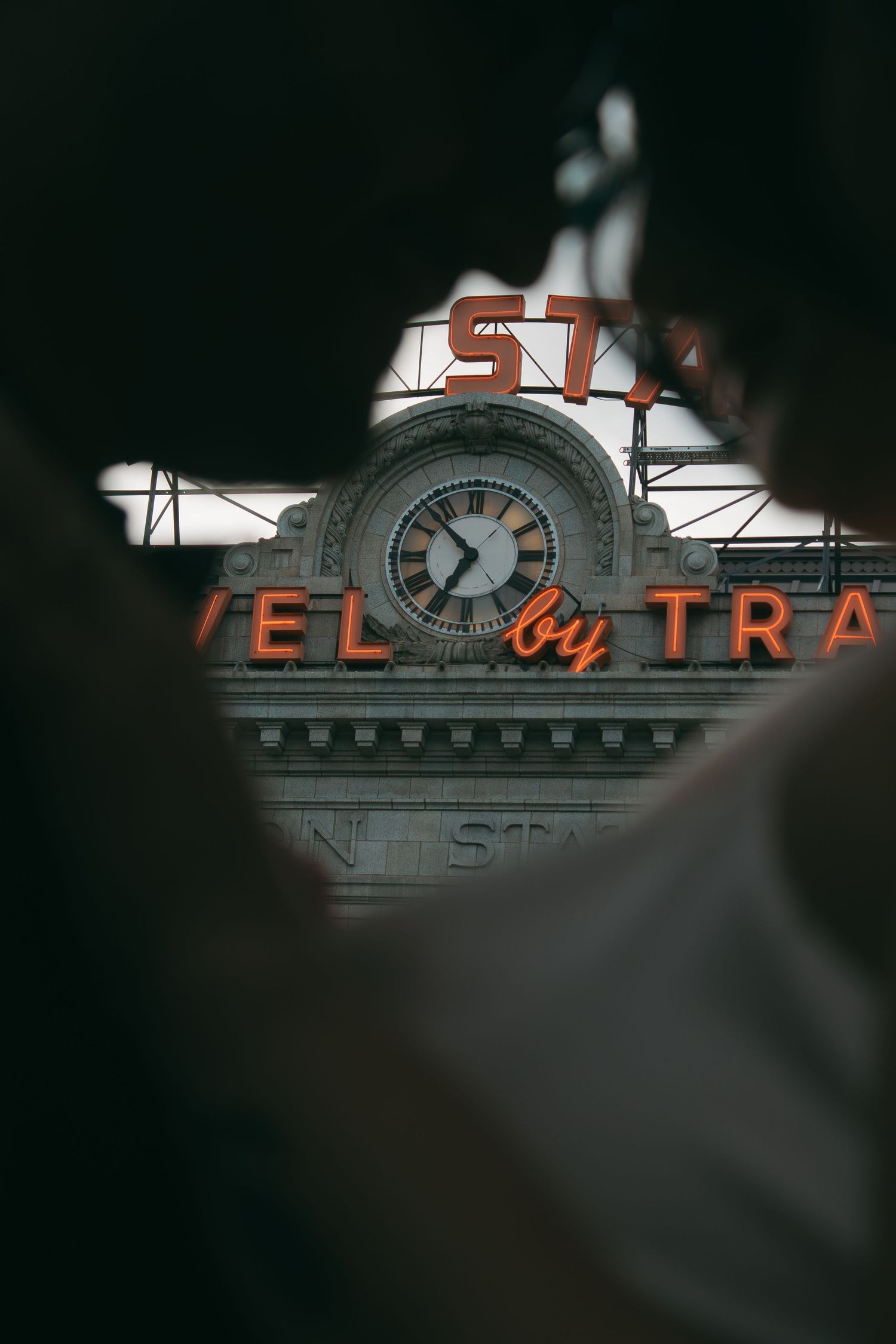 An artistic view of an illuminated vintage train station clock tower and signage against a dark background.