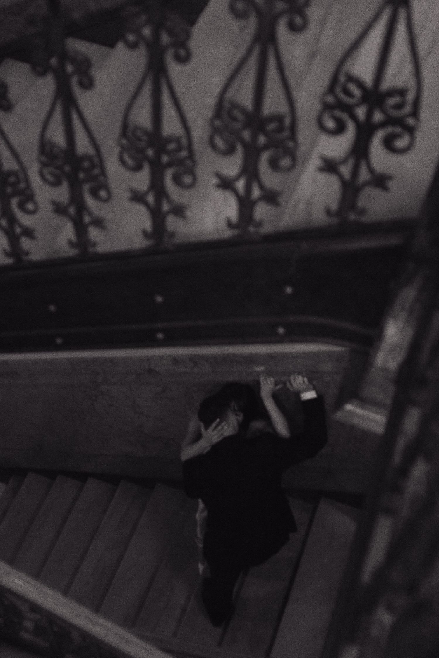 A dramatic black and white photo of ornate metal stair railings casting shadows in moody lighting.