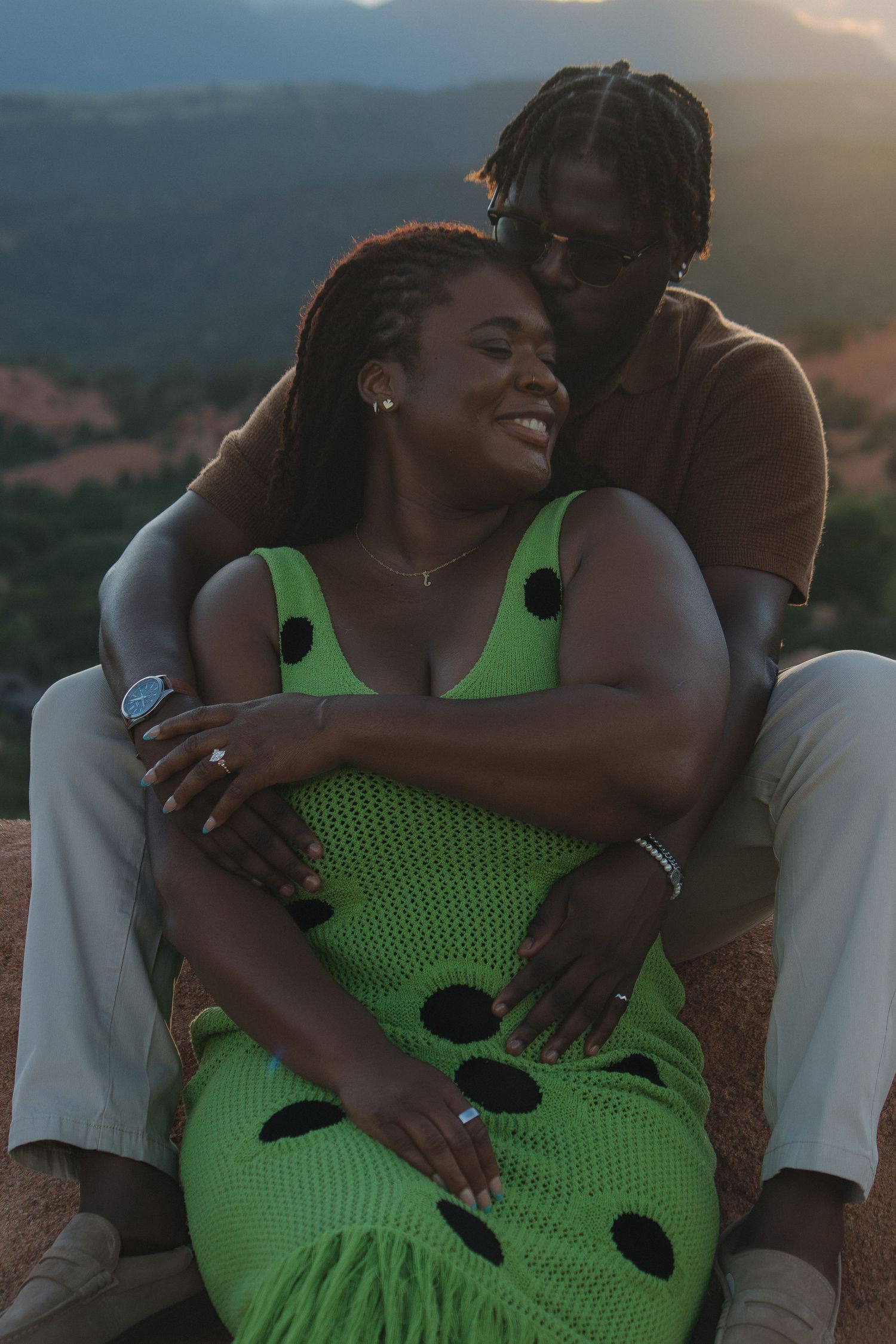 Intimate couple embracing on mountainside at sunset with bright green polka dot dress.