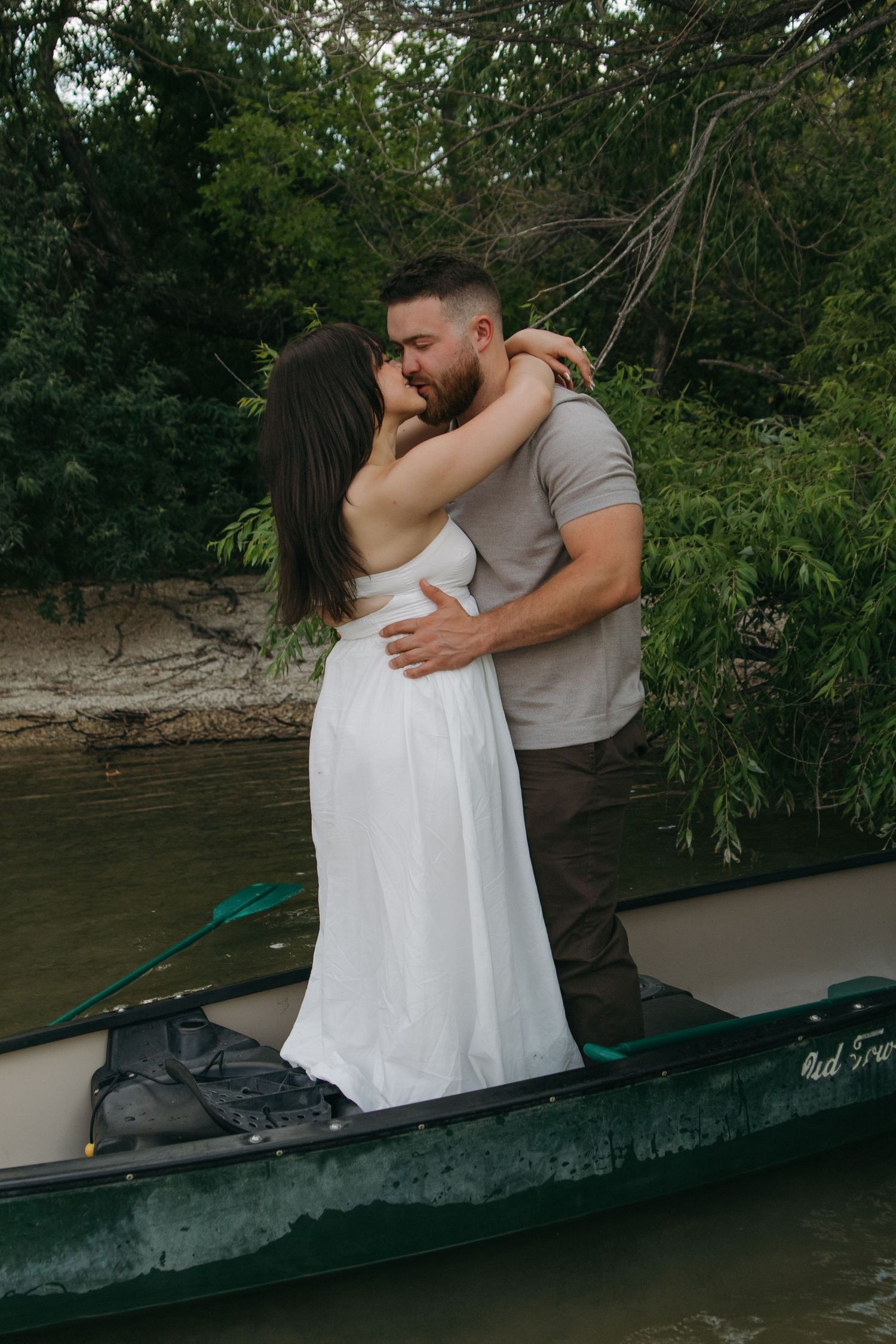 Two people embrace tenderly while sitting in a canoe on peaceful waters.