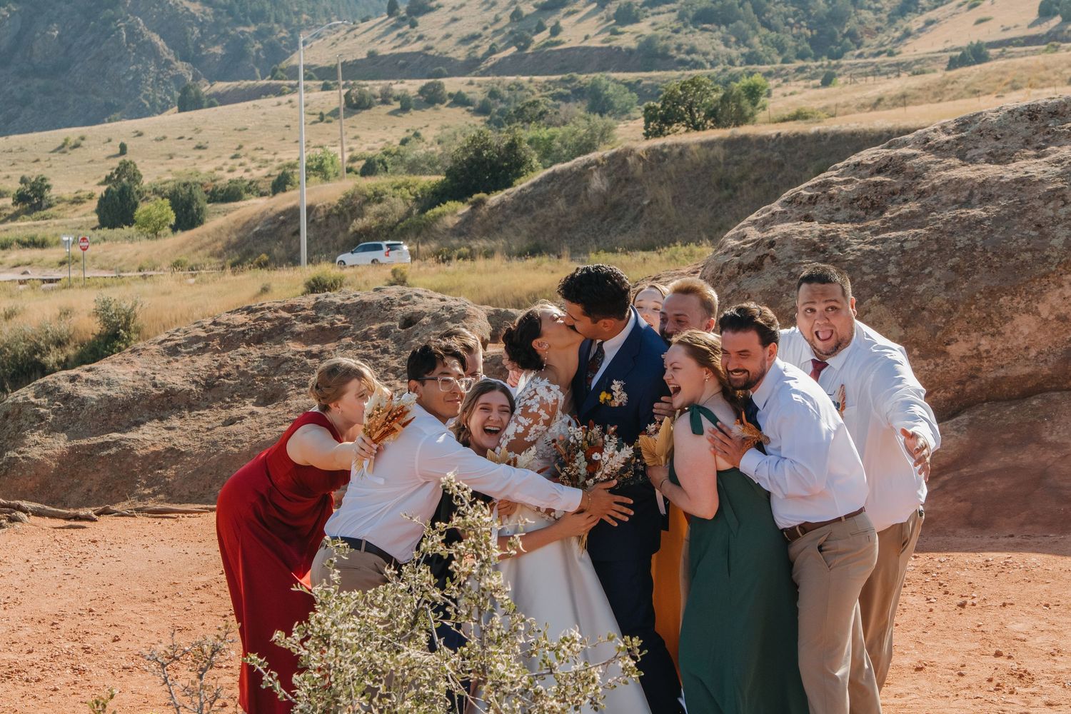 Wedding party celebrates joyfully on red rocks with mountains in the backdrop.