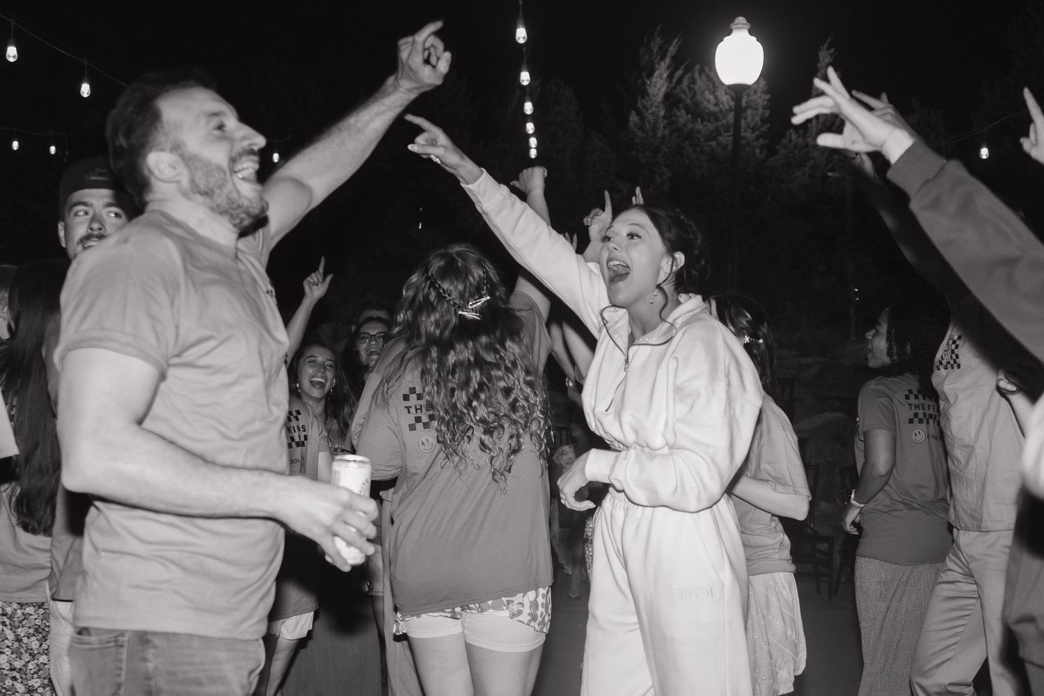 Reception guests dancing enthusiastically at night under outdoor lighting.