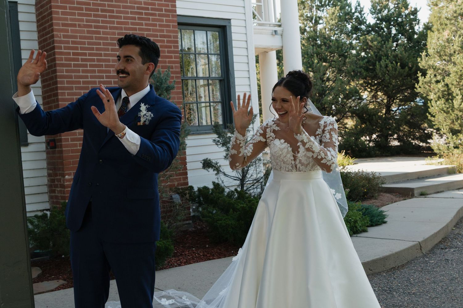Wedding party posing outside a white colonial style building with brick accents.