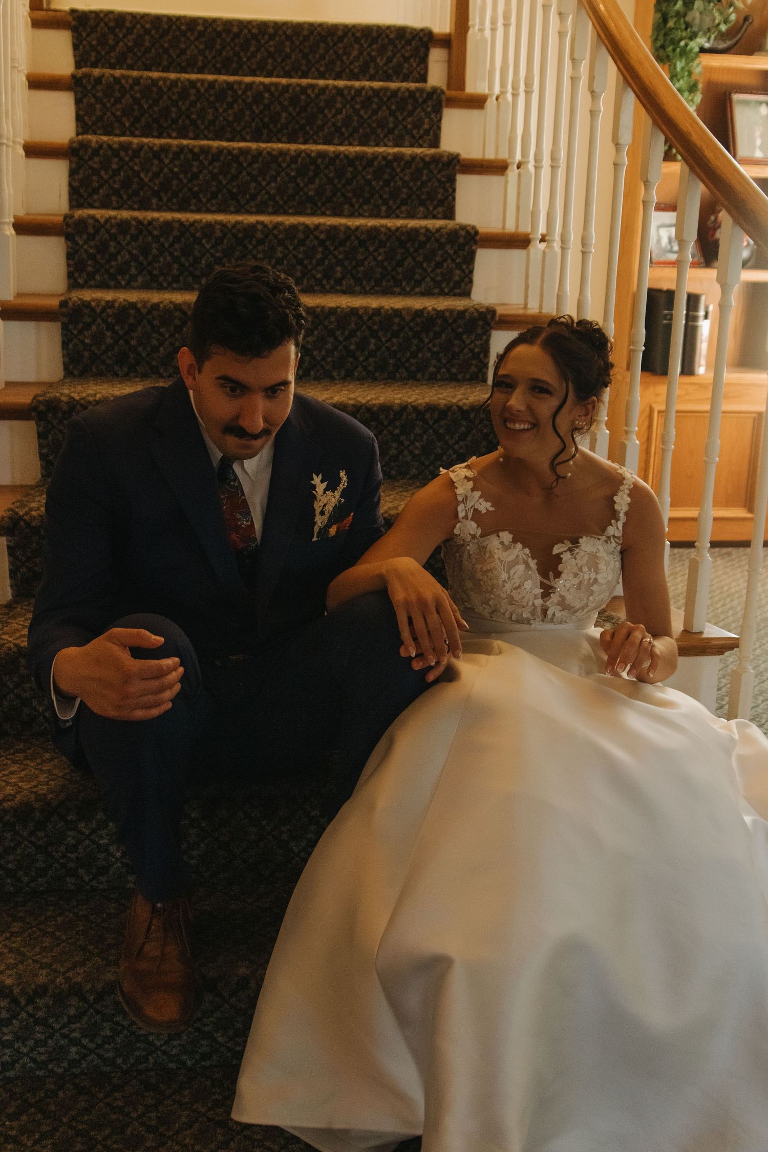 Wedding couple sitting together on patterned carpet staircase indoors.