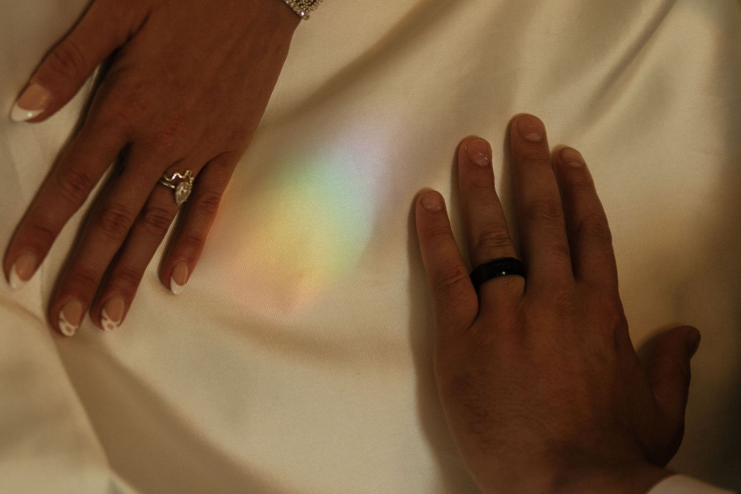 Wedding rings sparkle on hands against soft neutral background.