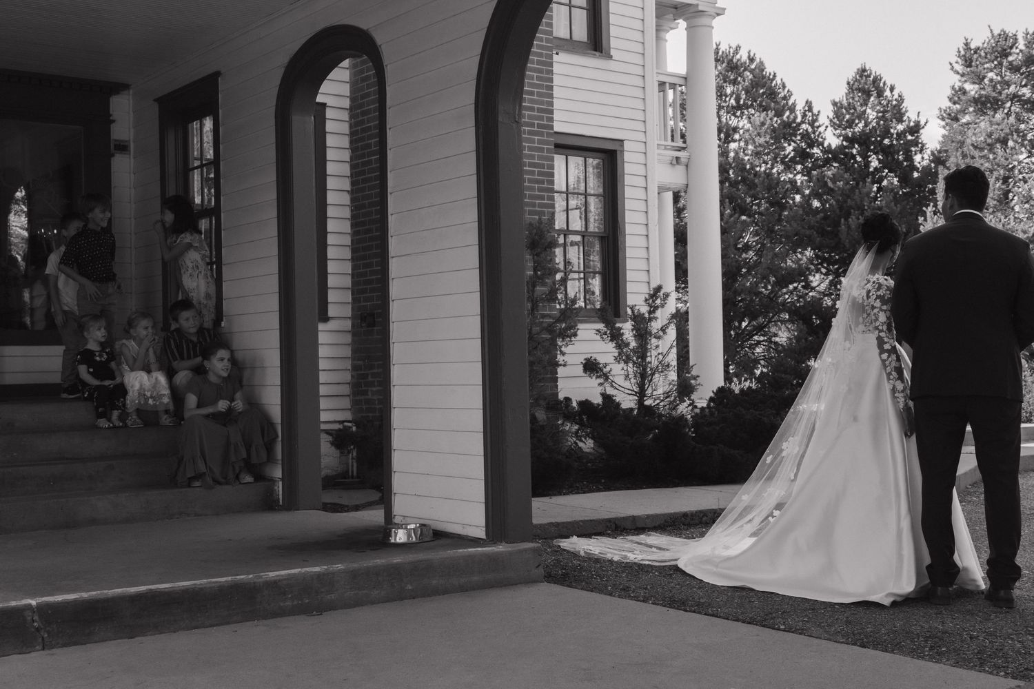 A black and white panoramic photo of a couple walking on a porch or veranda with white columns and railings.