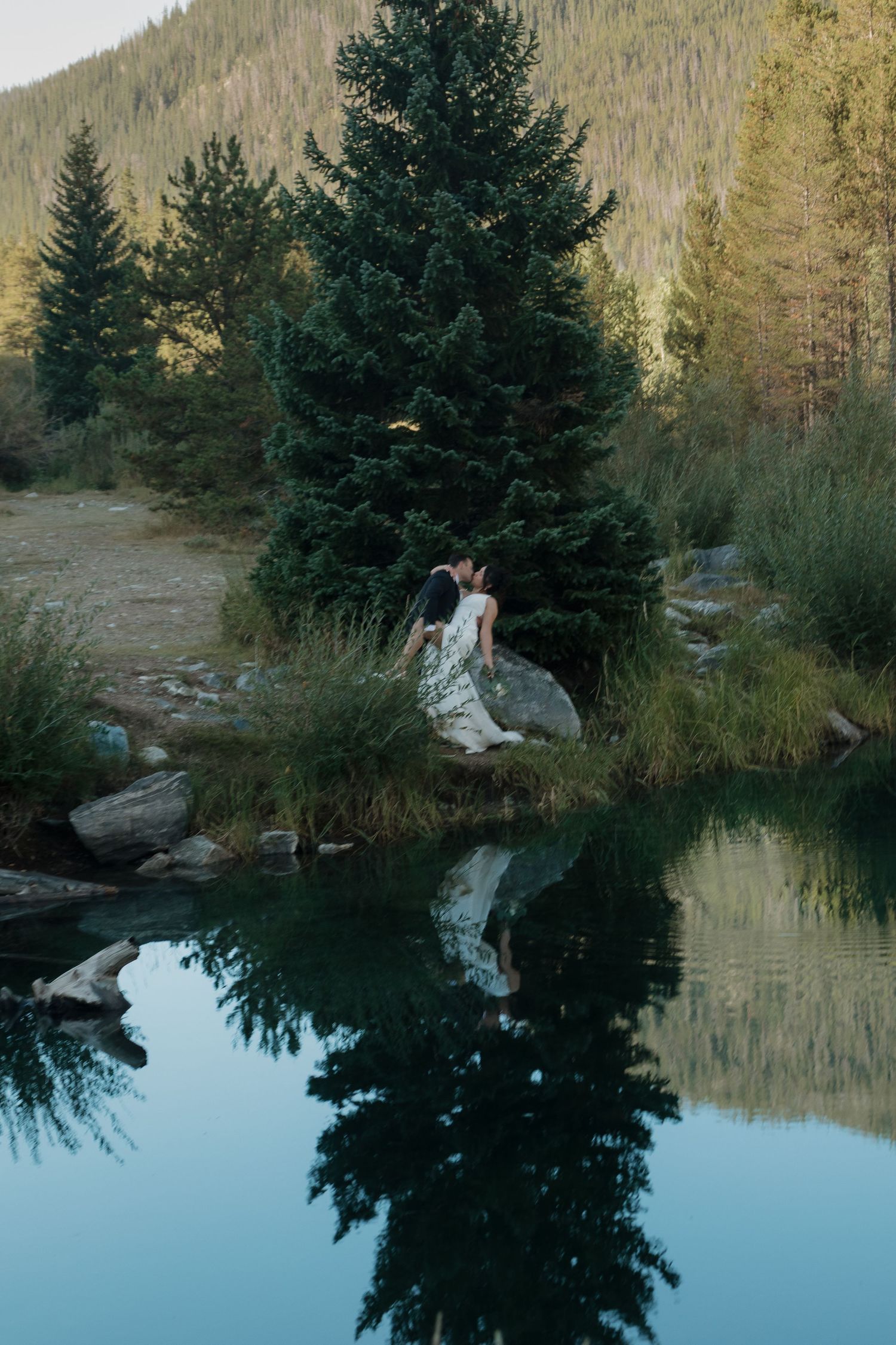 A serene mountain lake reflects evergreen trees and rocky shores at sunset.