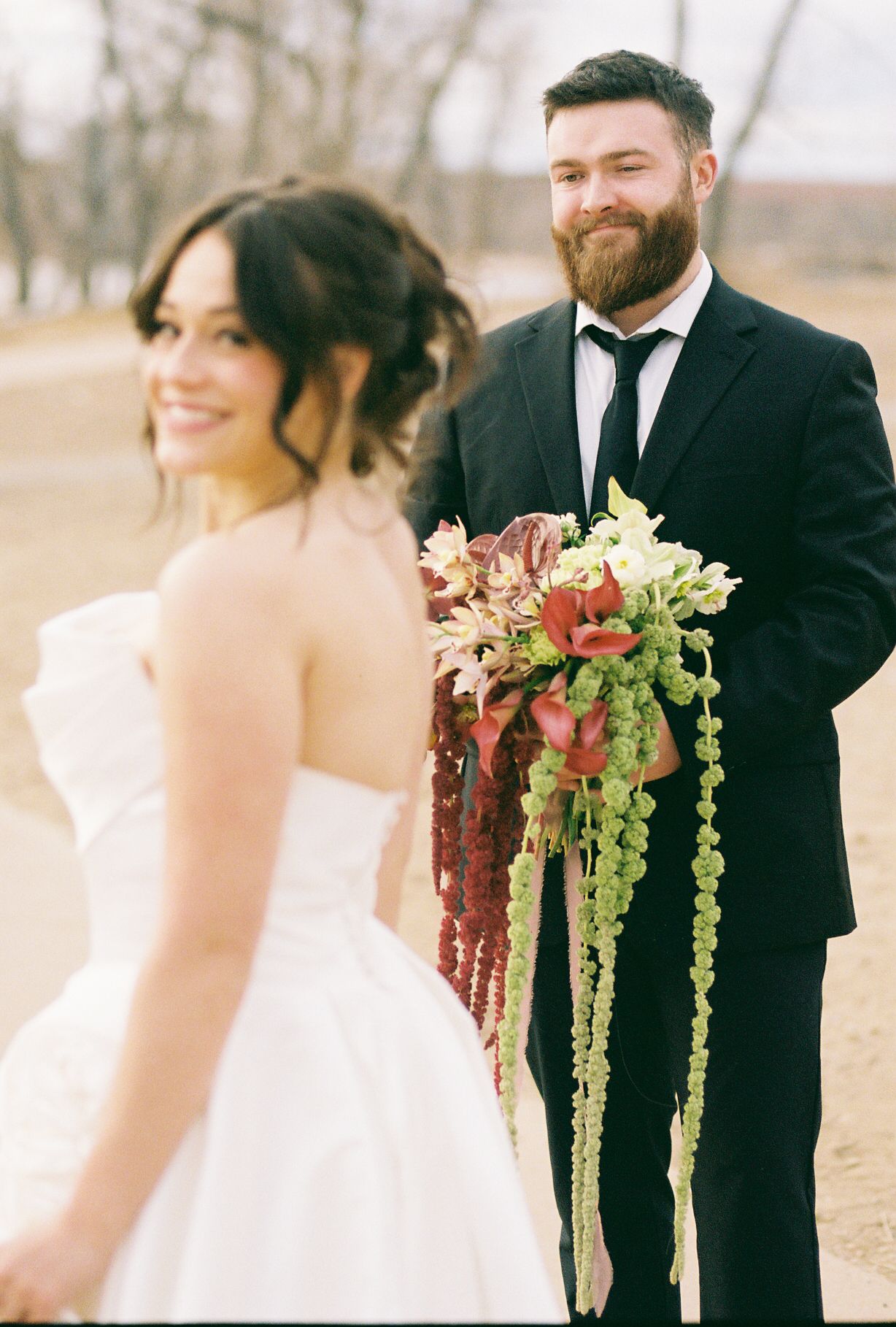 Wedding couple poses outdoors with dramatic burgundy and green cascading bouquet.