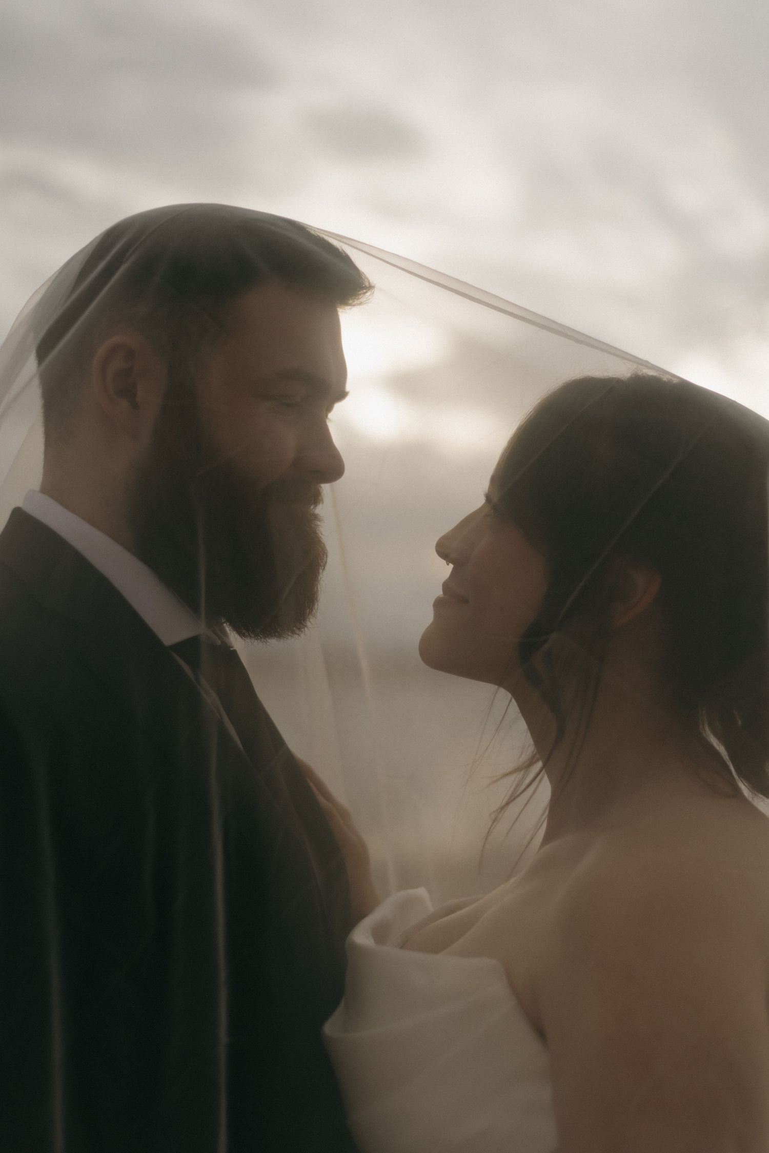 A wedding couple embraces under cloudy skies in an ethereal outdoor setting.