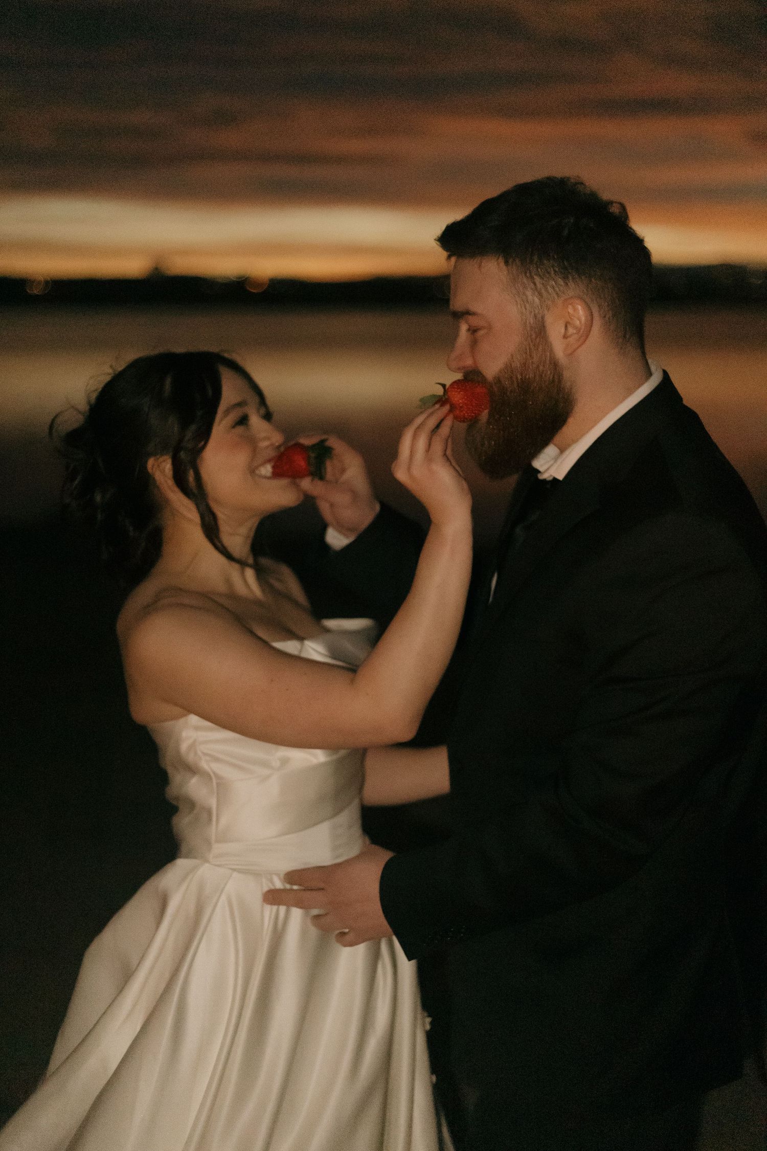 Intimate moment between newlyweds sharing dessert at sunset with warm golden lighting.