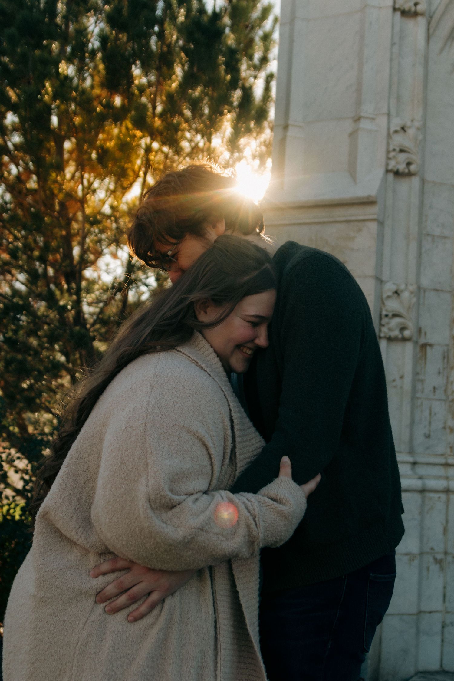 Intimate sunset engagement photos captured against a rustic white wall with warm backlighting.