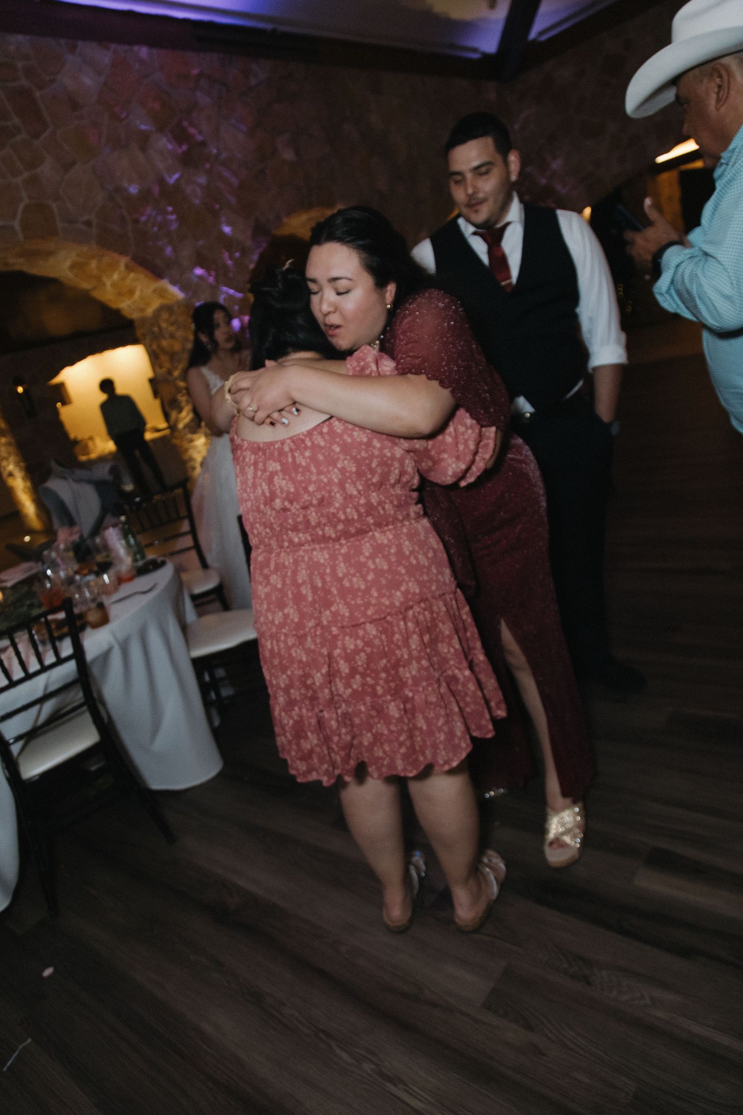 Couple dancing closely together at a lively wedding reception in a stone-walled ballroom.