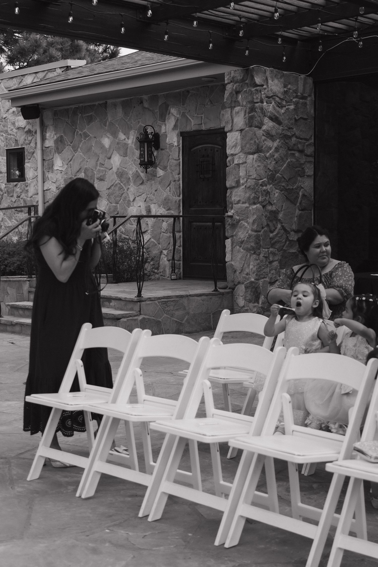 Photographer captures candid moment of children laughing at outdoor wedding ceremony with white folding chairs.