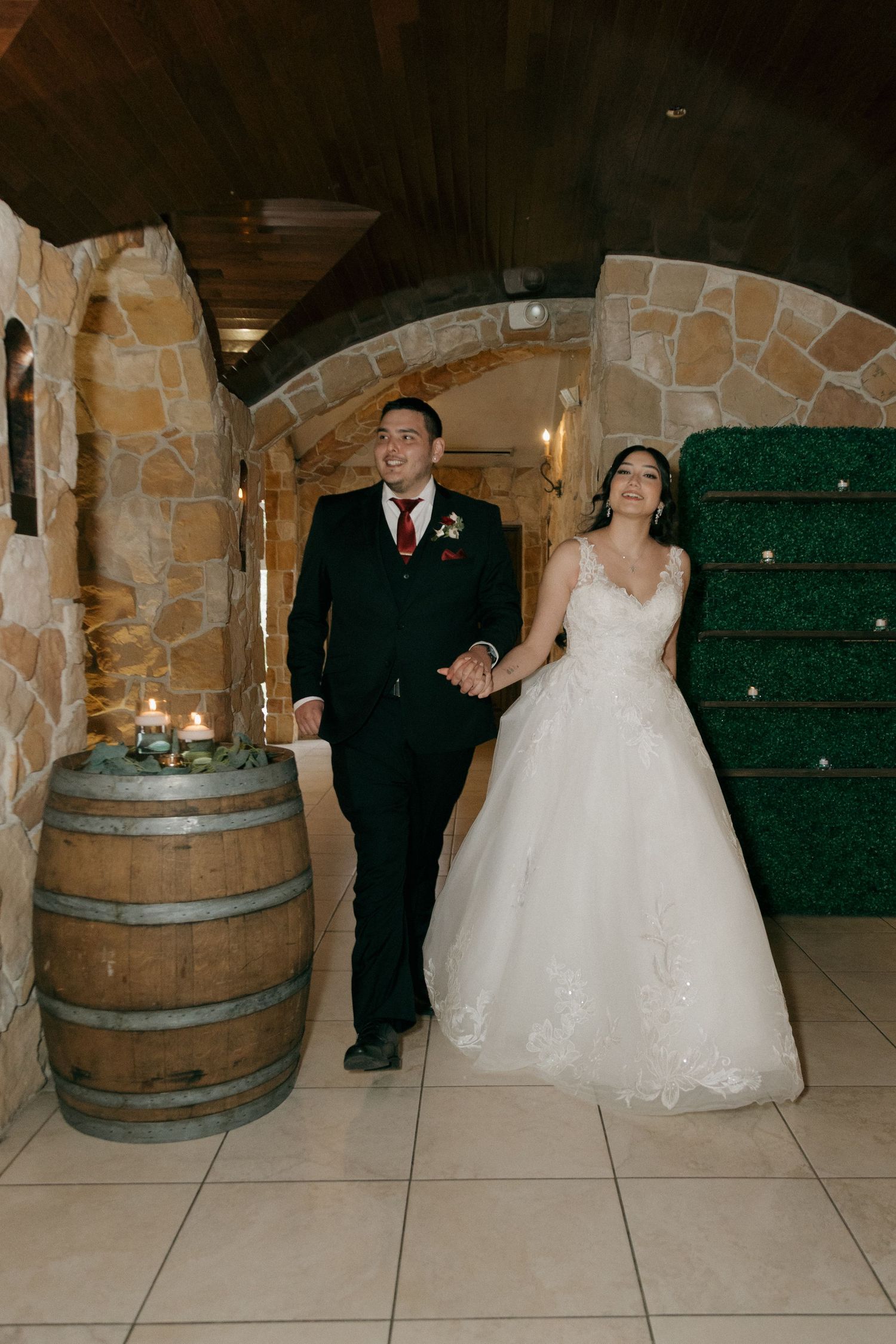 Bride and groom walking hand in hand through a rustic stone archway at their wedding venue.