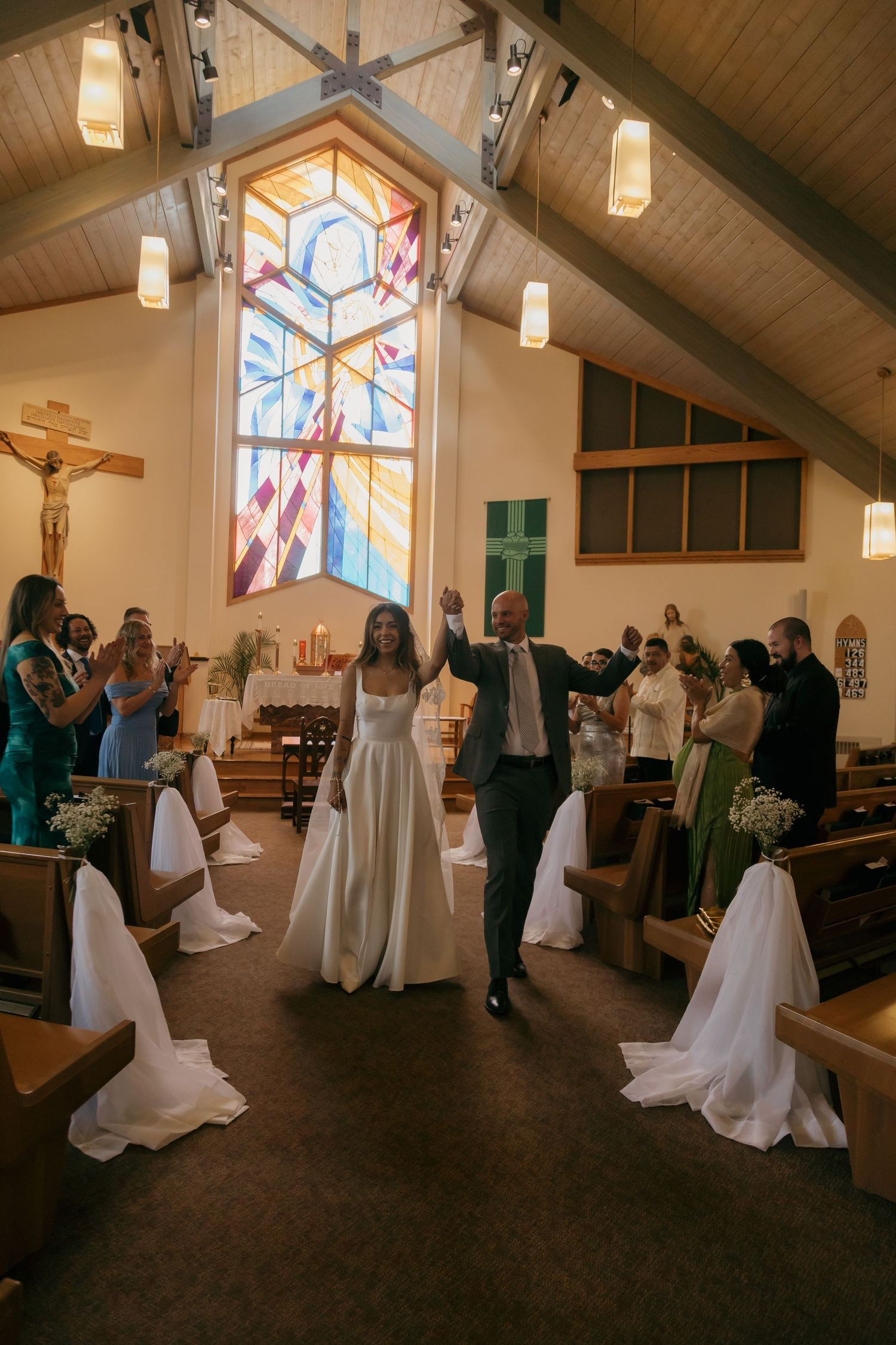 Newlyweds celebrate joyfully as they walk back down the aisle after their wedding ceremony in a sunlit church.