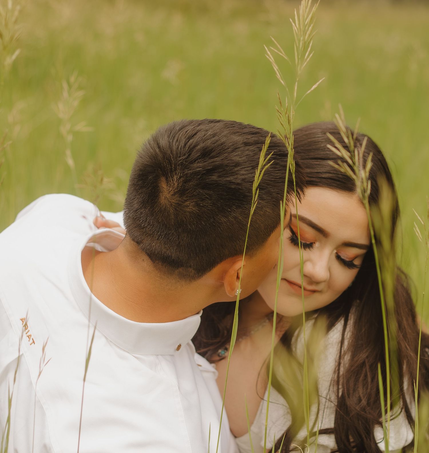 A romantic couple shares an intimate moment among tall grasses in a sun-lit meadow.