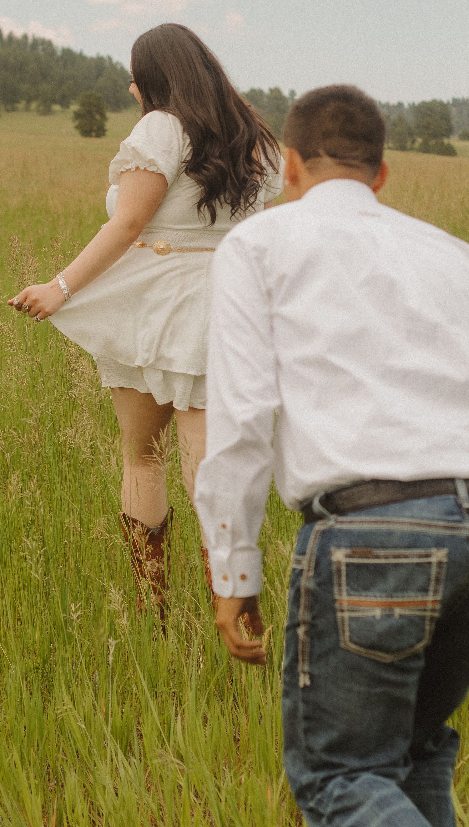 Romantic couple running through a golden meadow wearing white and denim.
