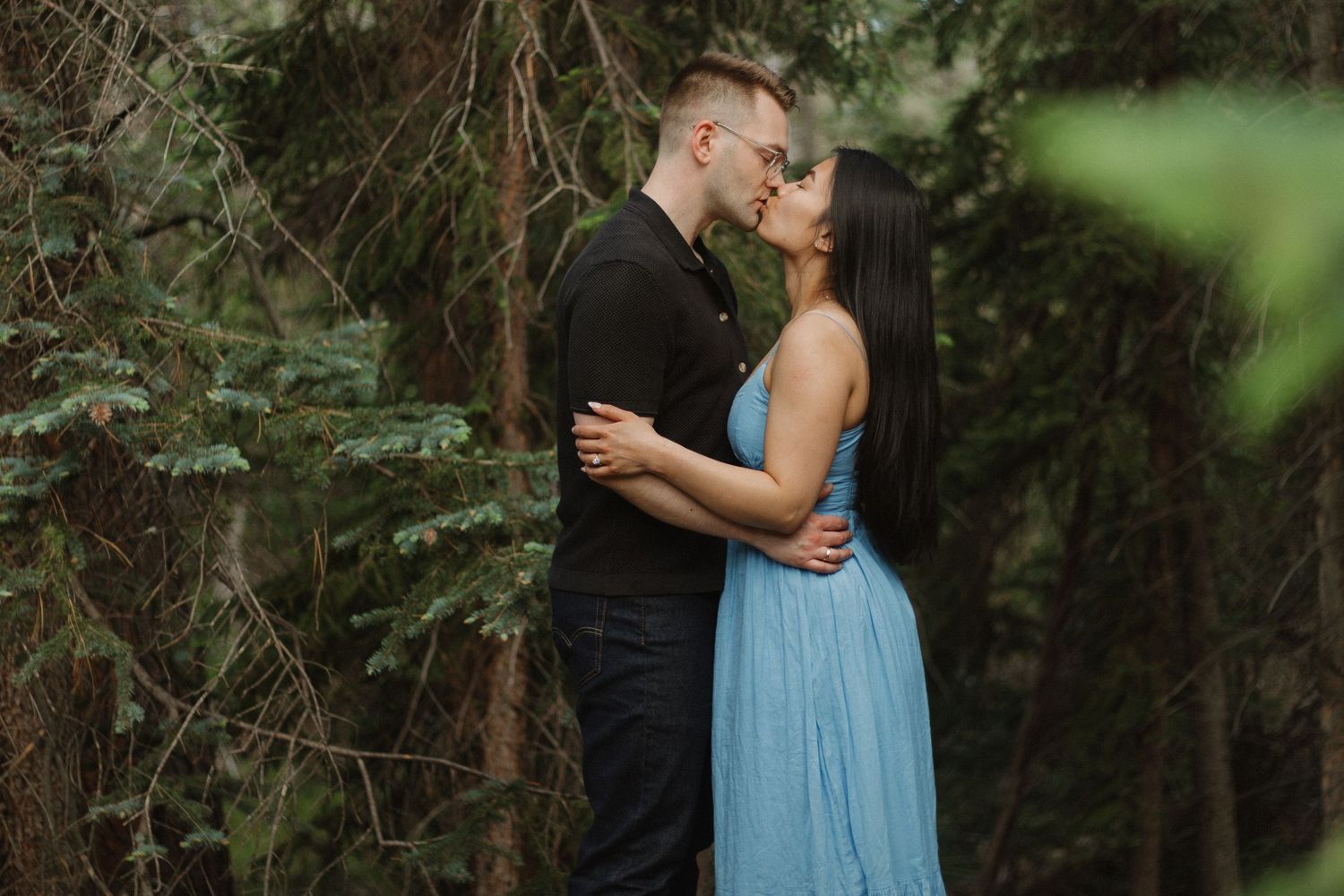 A tender embrace captured in a wooded setting with soft natural lighting.