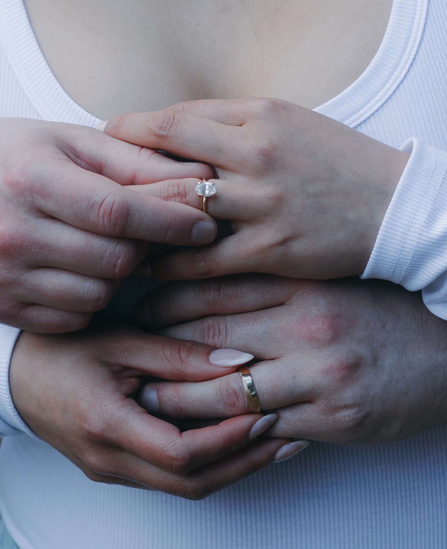 Close-up of hands wearing matching wedding rings against a white fabric background.