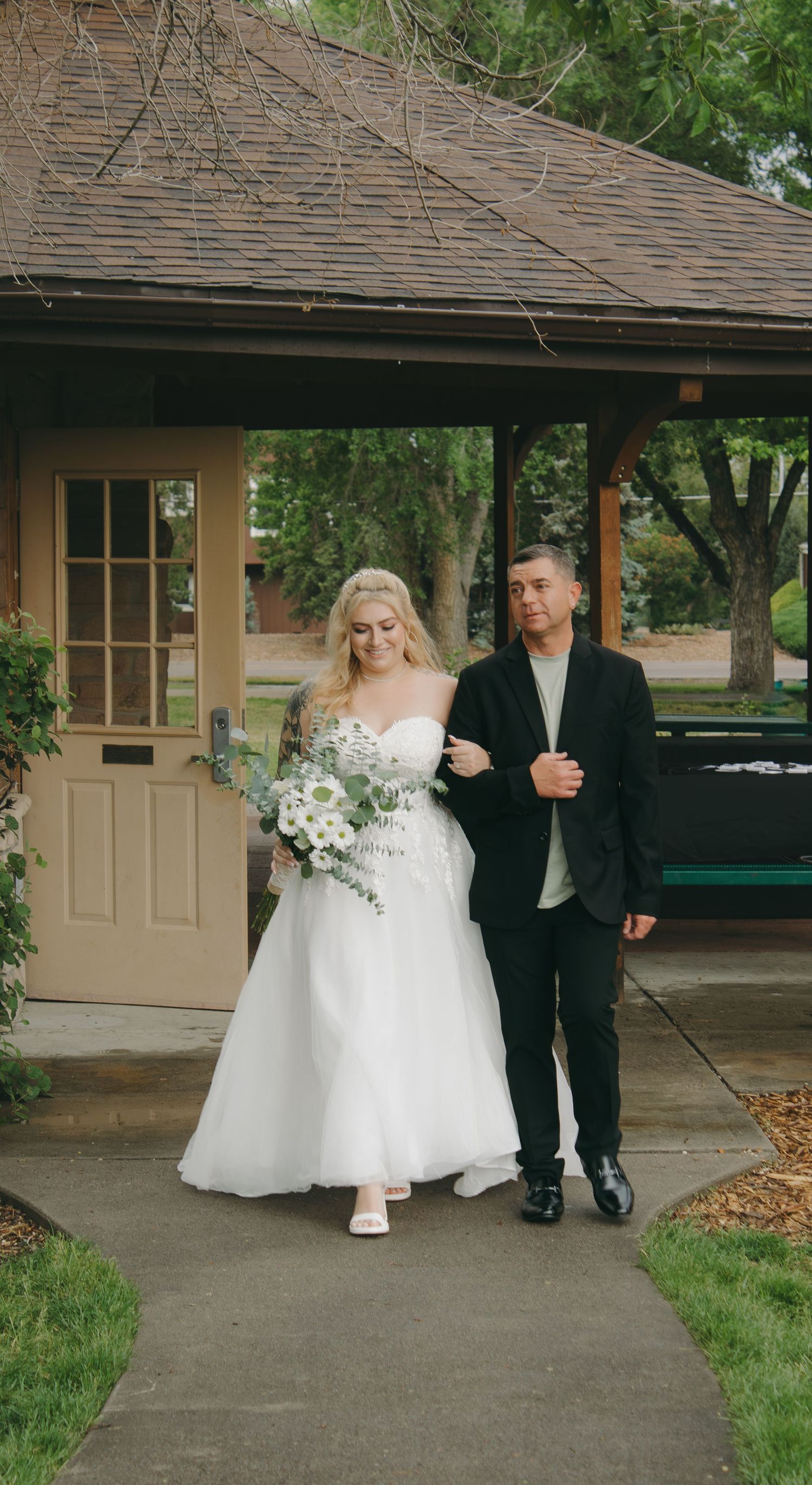 Bride in white dress walks with wedding party members under covered walkway.