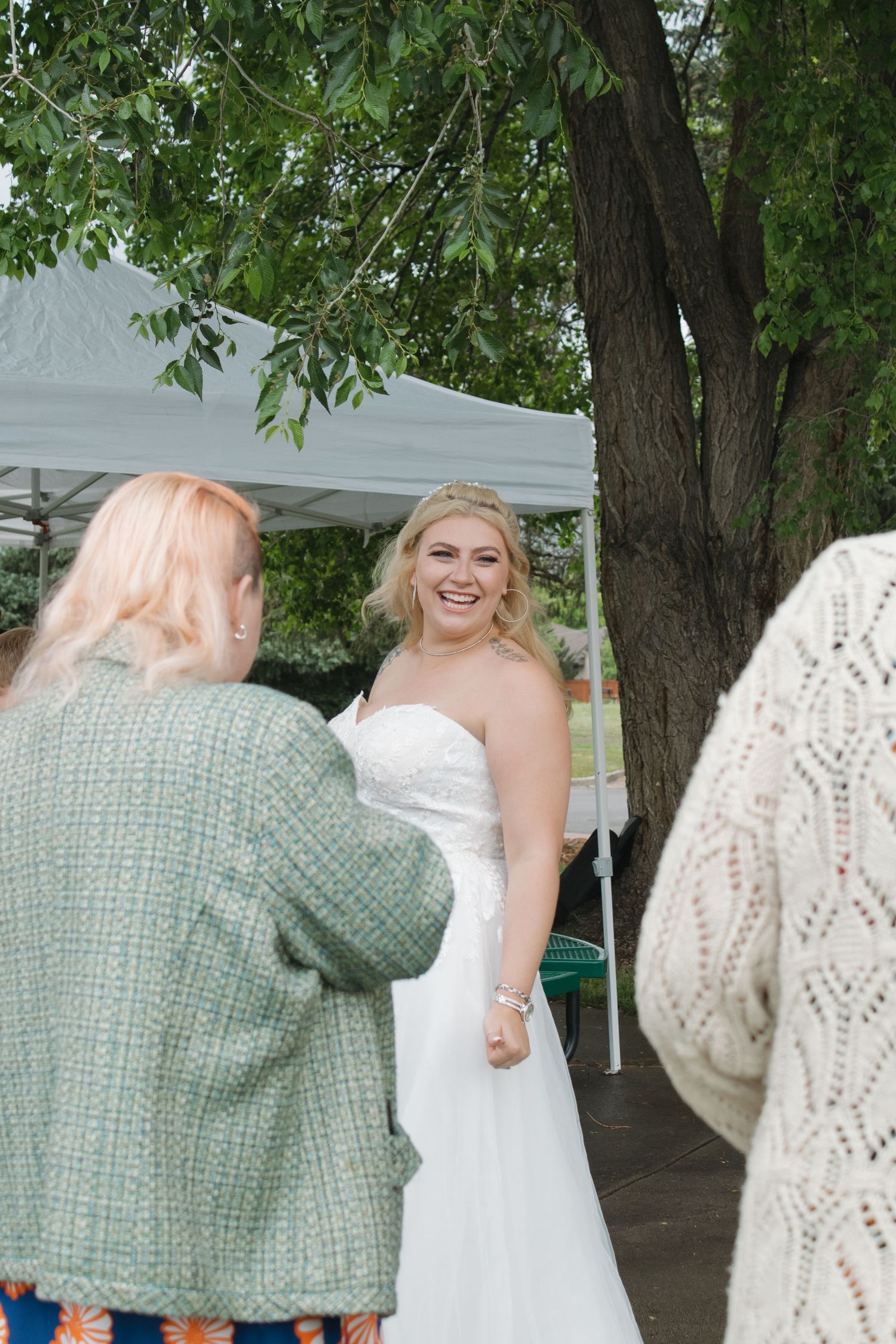 Wedding celebration scenes showing warm embraces under white tent with lush greenery in background.