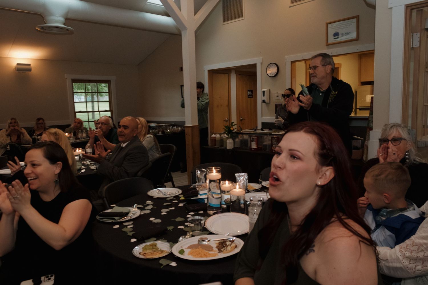 Wedding guests enjoying meal at reception tables with dark tablecloths.