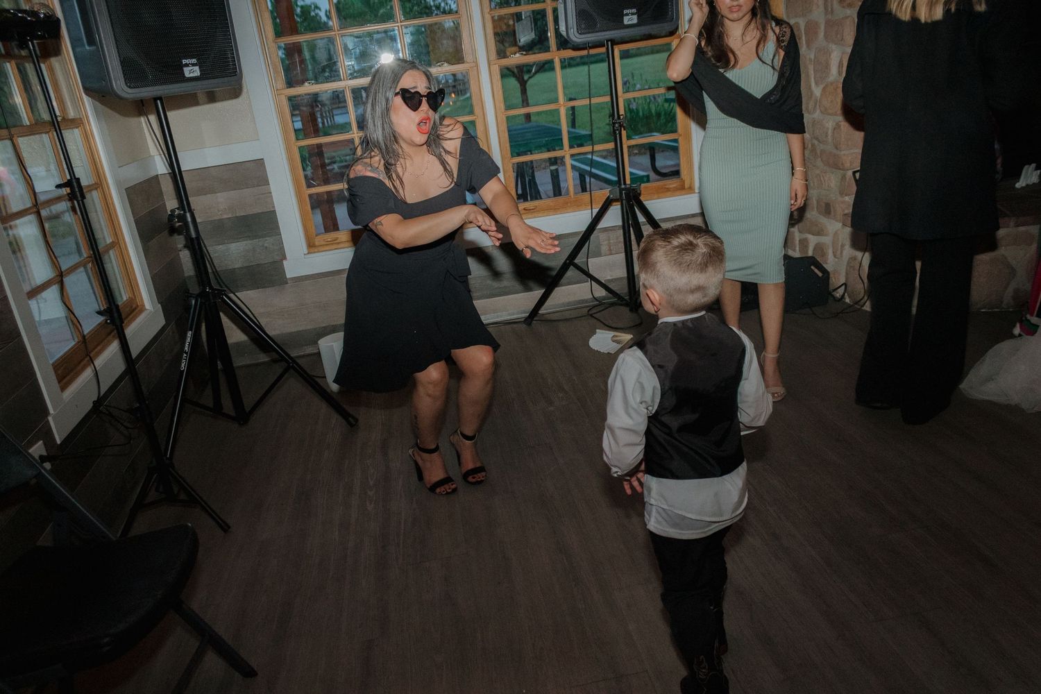 Wedding guests dancing in a rustic venue with wooden windows and stone walls.