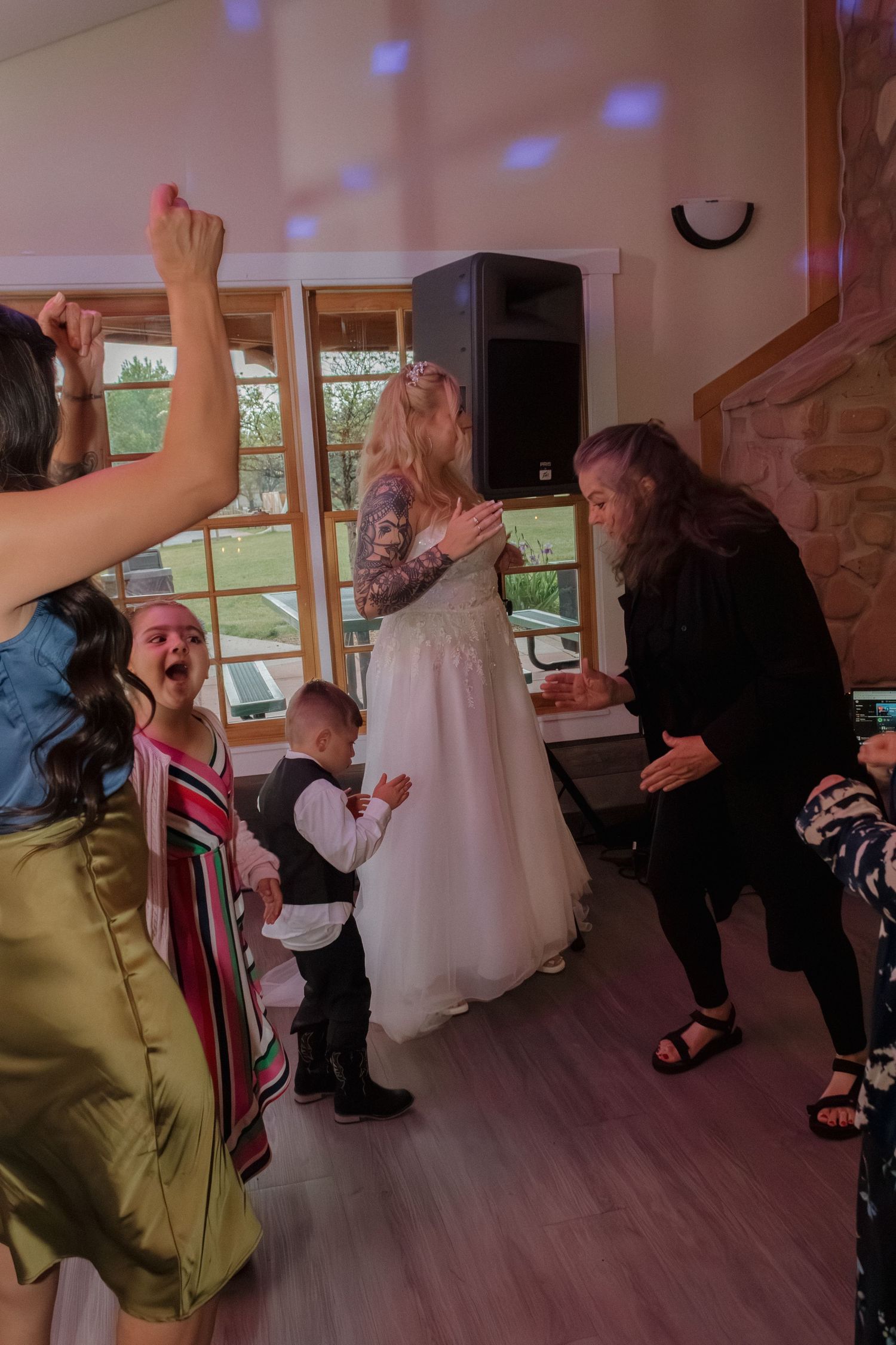 Wedding guests dancing and celebrating on wooden dance floor under blue lighting.