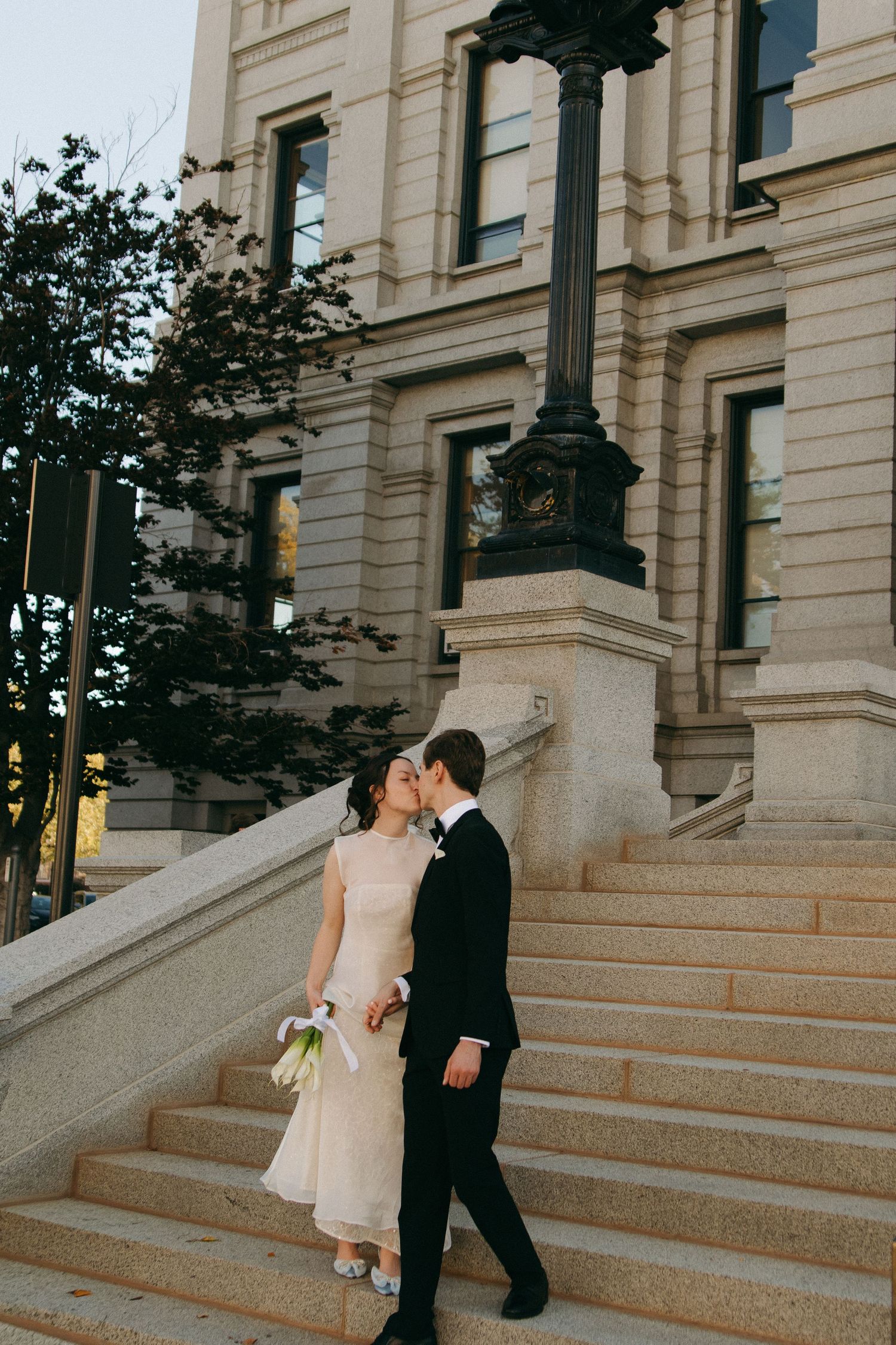 A wedding couple sharing intimate moments on stone steps of a grand building.