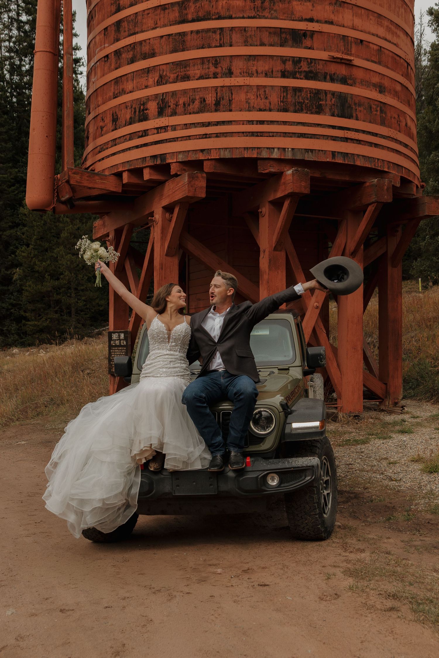 Wedding couple relaxes beneath a large wooden water tower structure in a natural setting.