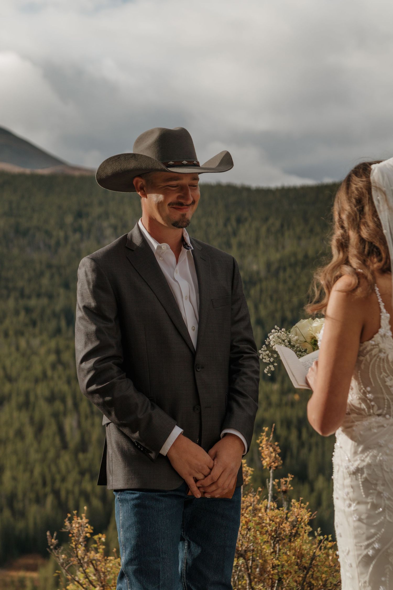 A couple shares a joyful moment during their mountain wedding ceremony with evergreen forests in the background.
