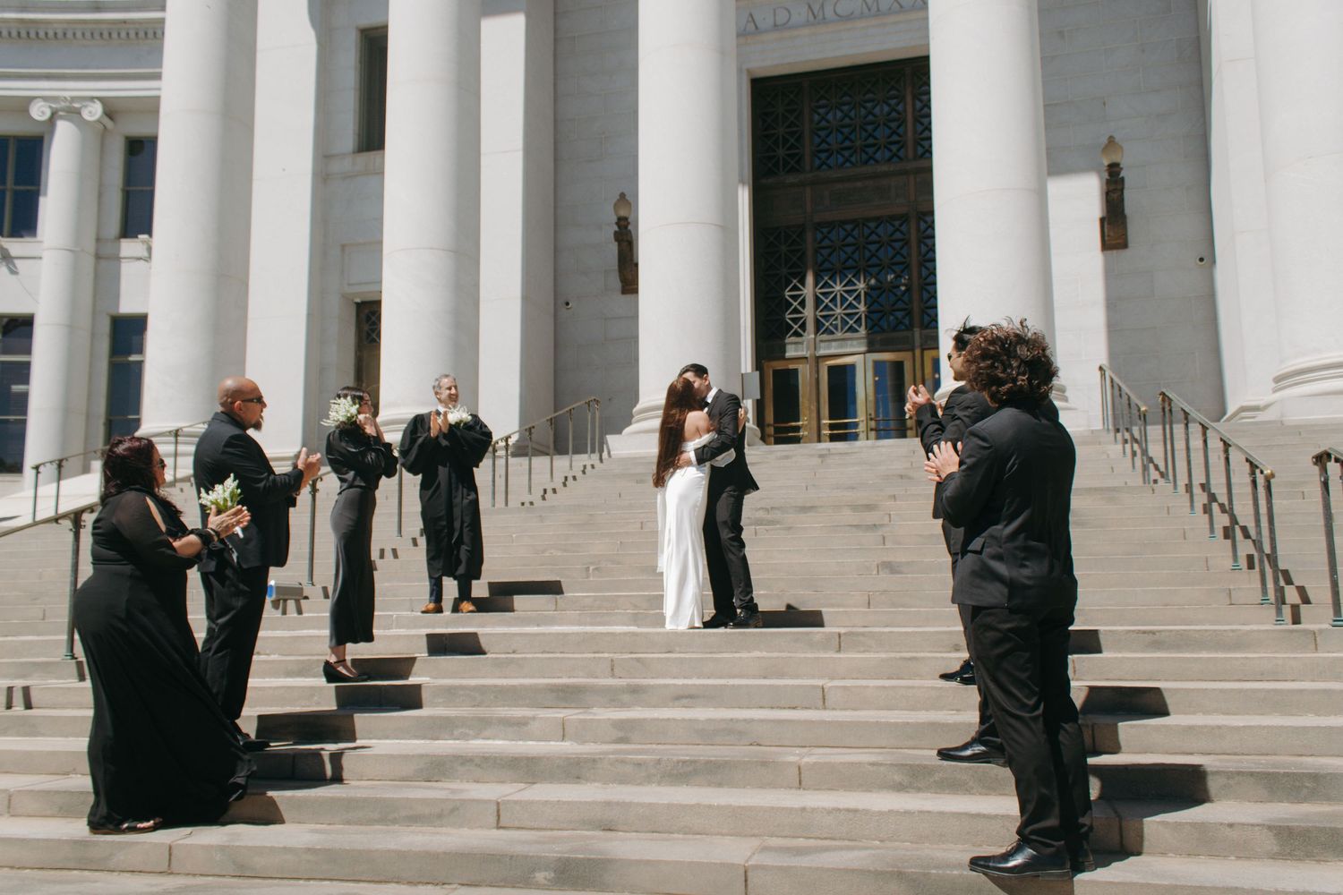 A photographer captures a wedding moment on the grand steps of a courthouse with white columns and formal attire.