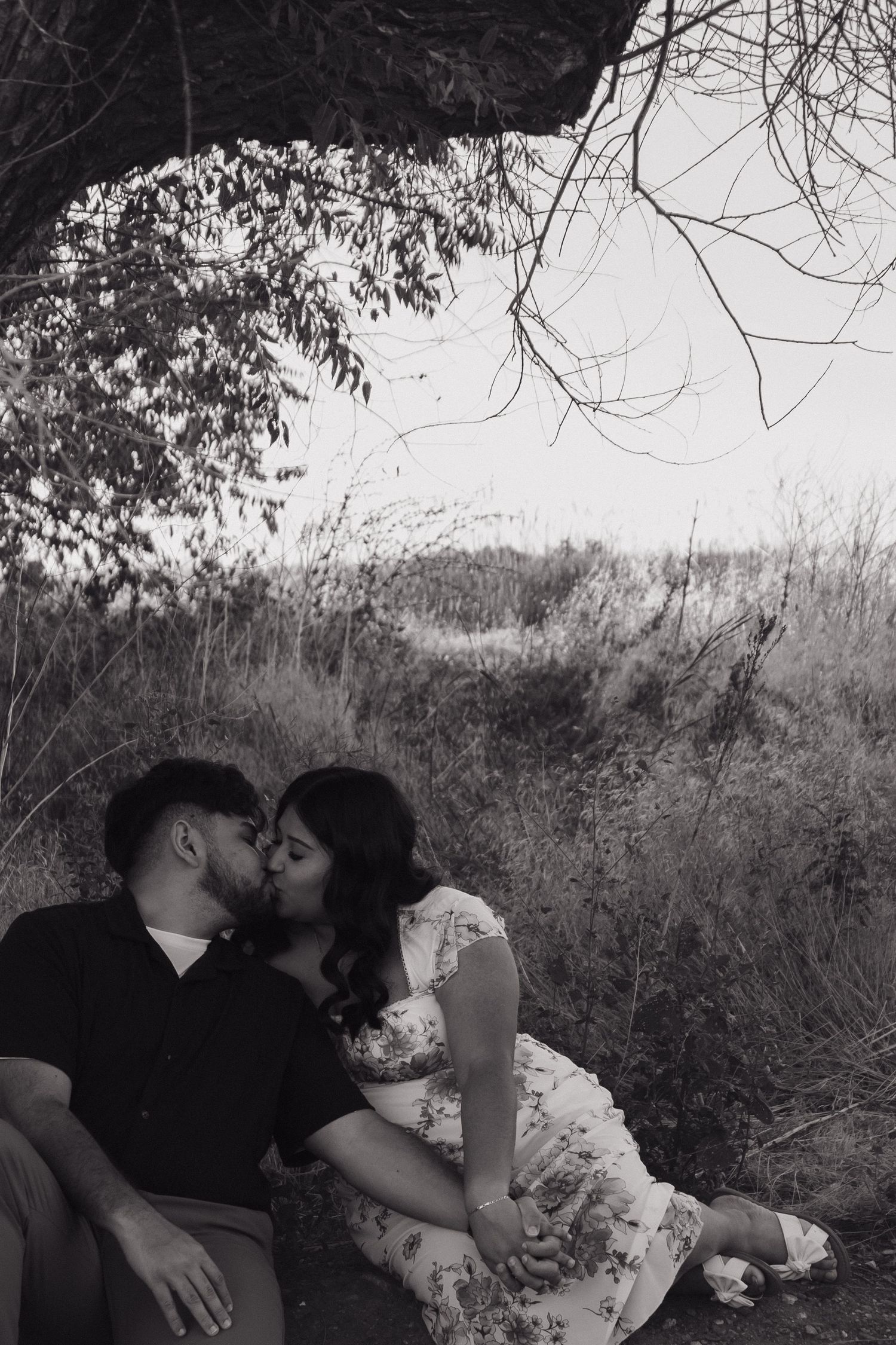 A romantic black and white portrait of a couple sharing an intimate moment under a tree.