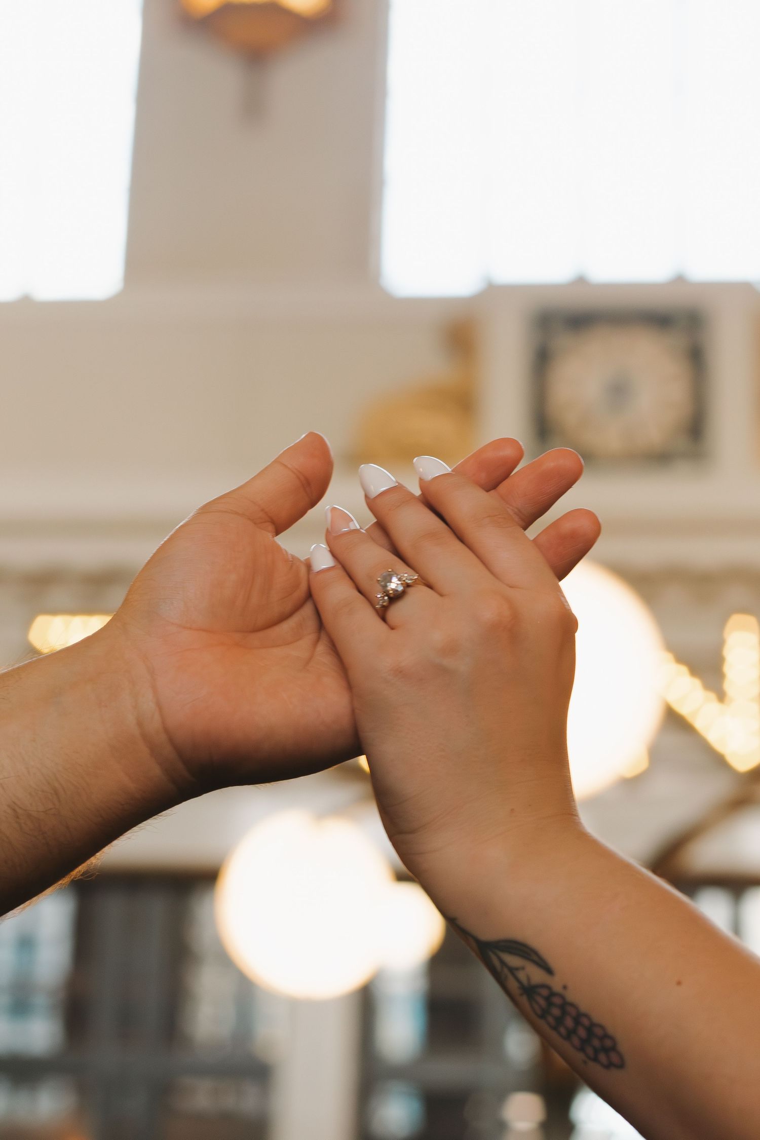 Close-up of hands with engagement rings intertwined against a bright background.